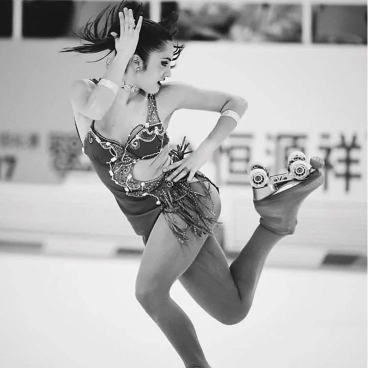 Uma mulher patinando no gelo usando traje de dança, com cabelo solto ao vento, em uma pista de gelo.