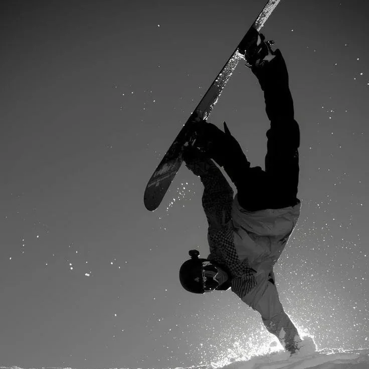 Pessoa praticando snowboard na neve, realizando uma manobra inclinada para baixo.