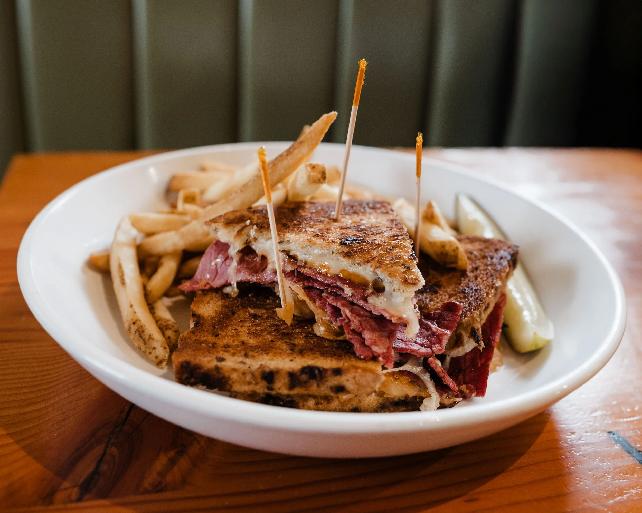 A classic Reuben sandwich served with French fries and a pickle spear.