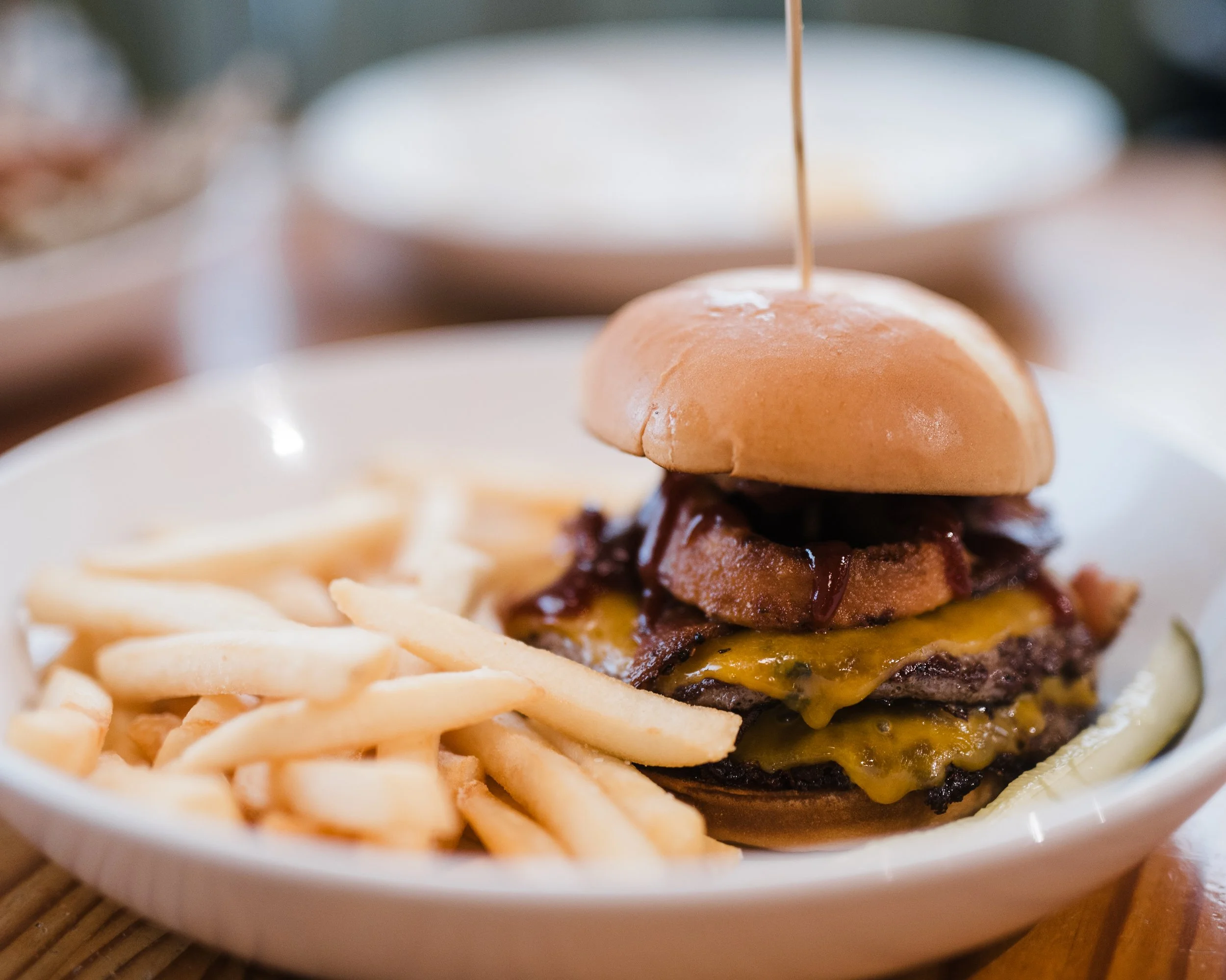 A Double Western burger with barbecue sauce and an onion ring alongside crispy French fries.