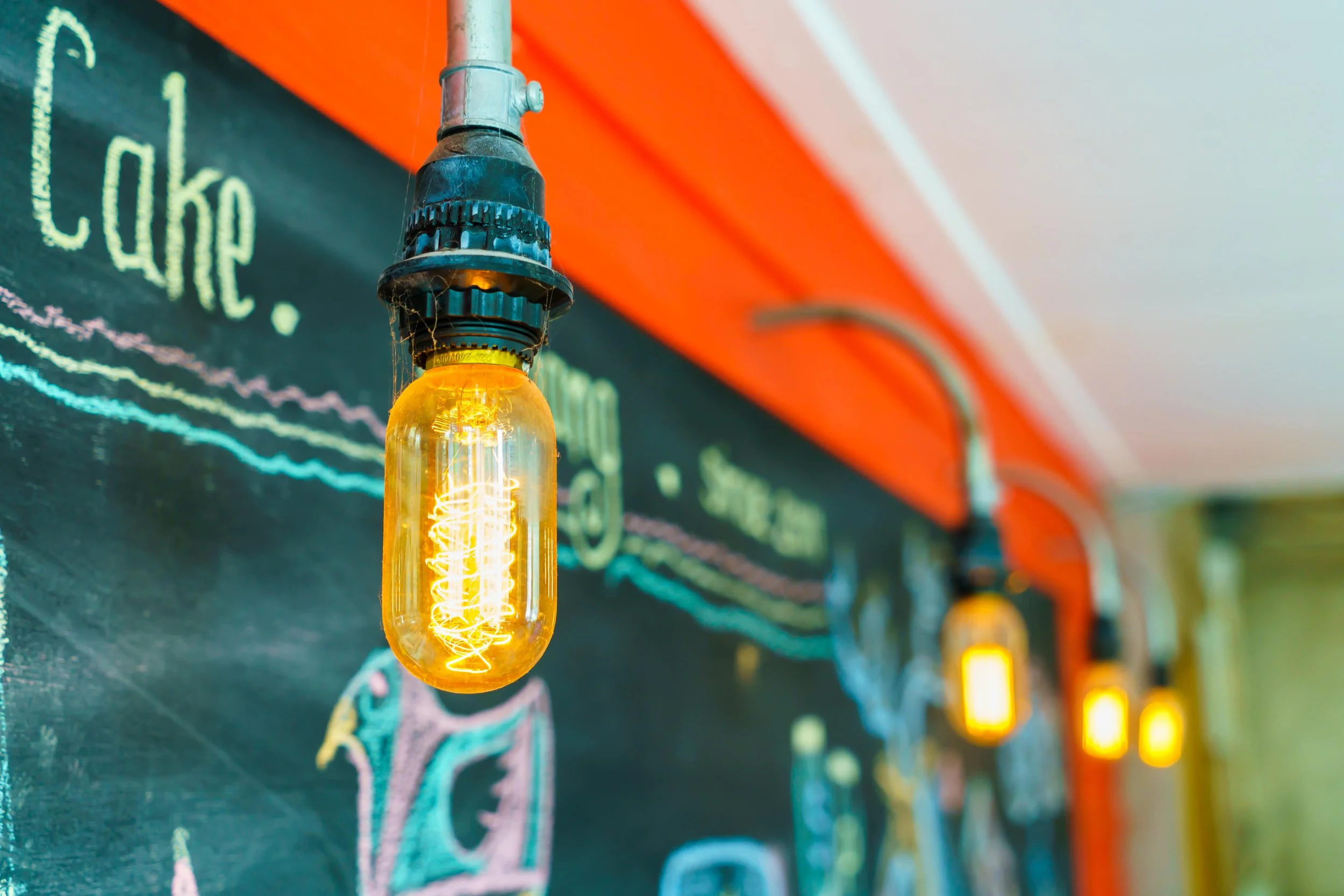 Close-up of vintage Edison-style filament light bulbs hanging against a colorful wall with chalkboard art.