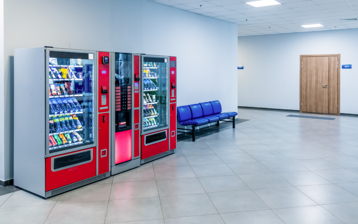 Indoor hallway with two vending machines, a row of blue chairs, and a wooden door.