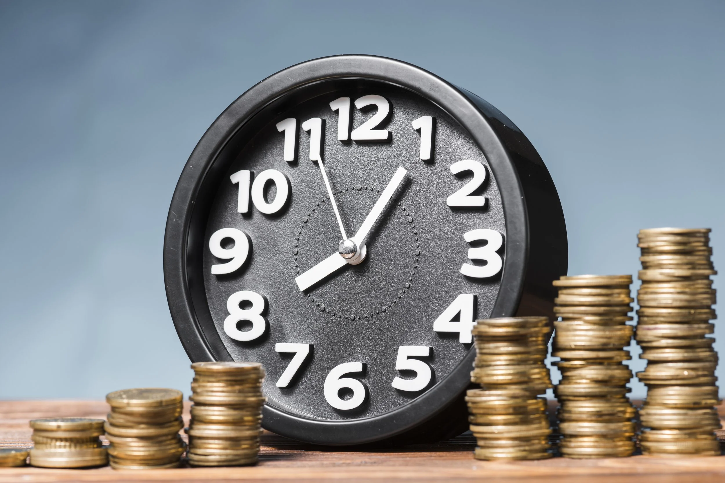 A black clock showing 9:02 with stacks of gold coins arranged in the foreground.