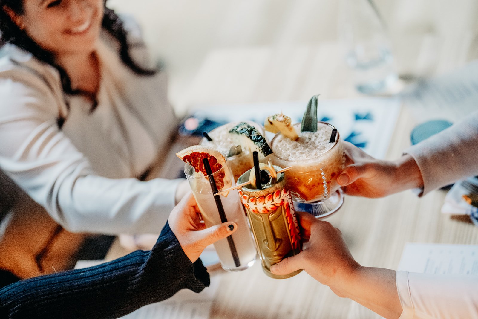 Group of people clinking cocktails with garnishes in a toast, seen from above in a social setting.