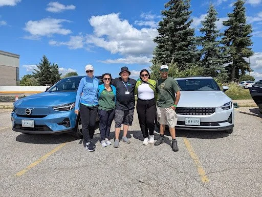 ecoCaledon members and EV Revolution members standing in front of electric cars, smiling