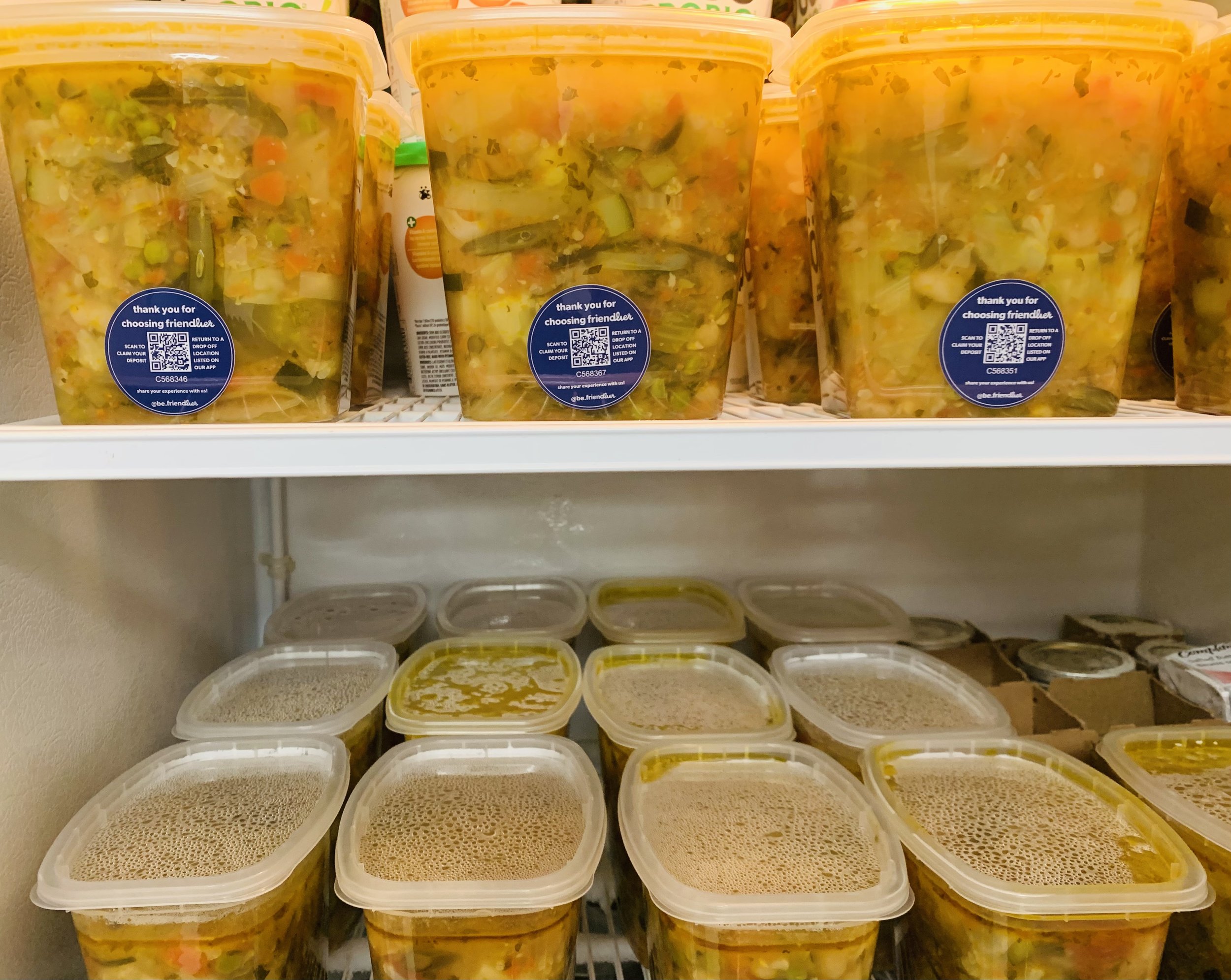Plastic containers of food lined up in fridge with stickers and barcodes on them