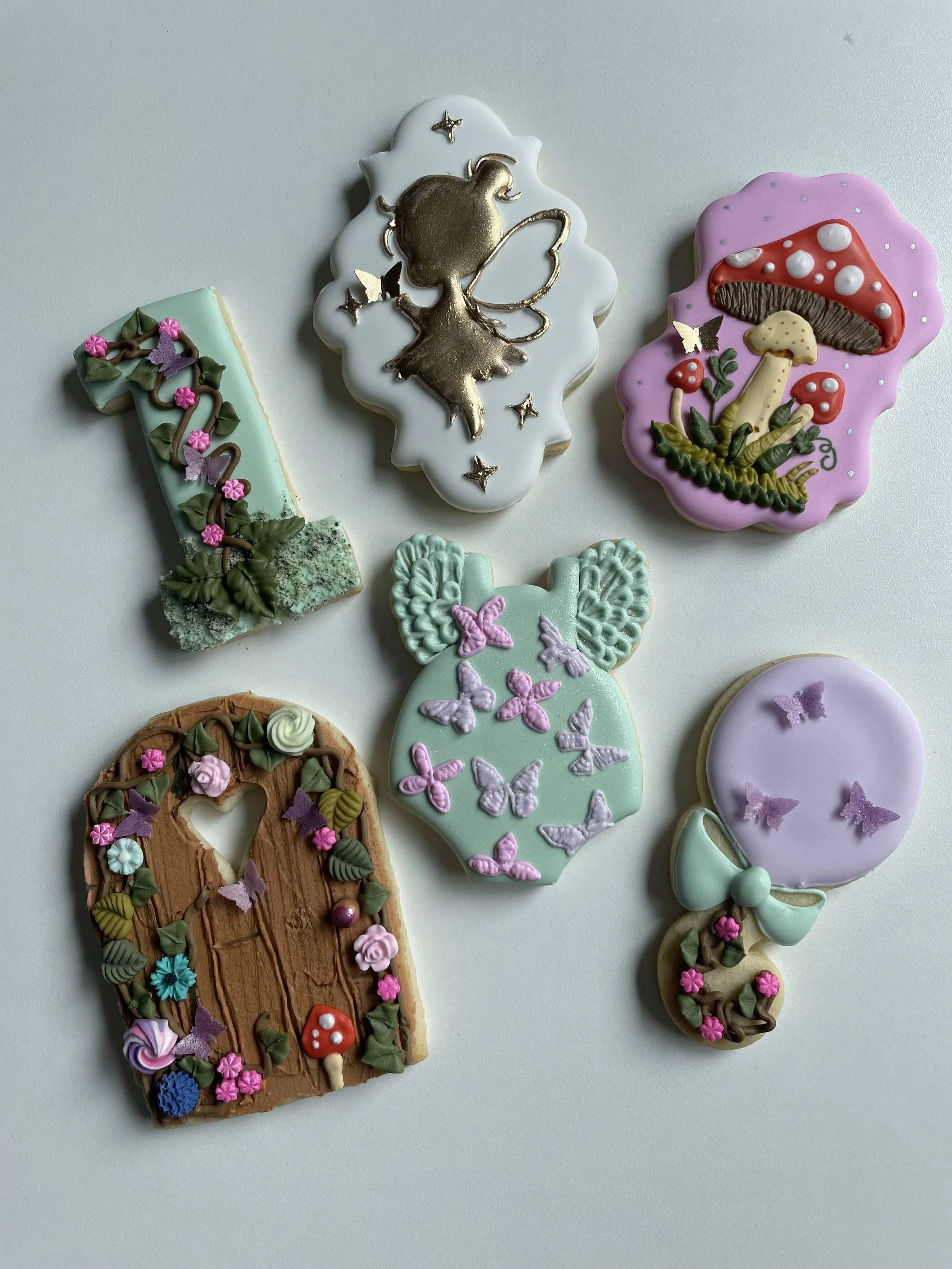 Decorated cookies with fairy, mushrooms, door, and butterfly themes in pastel colors.