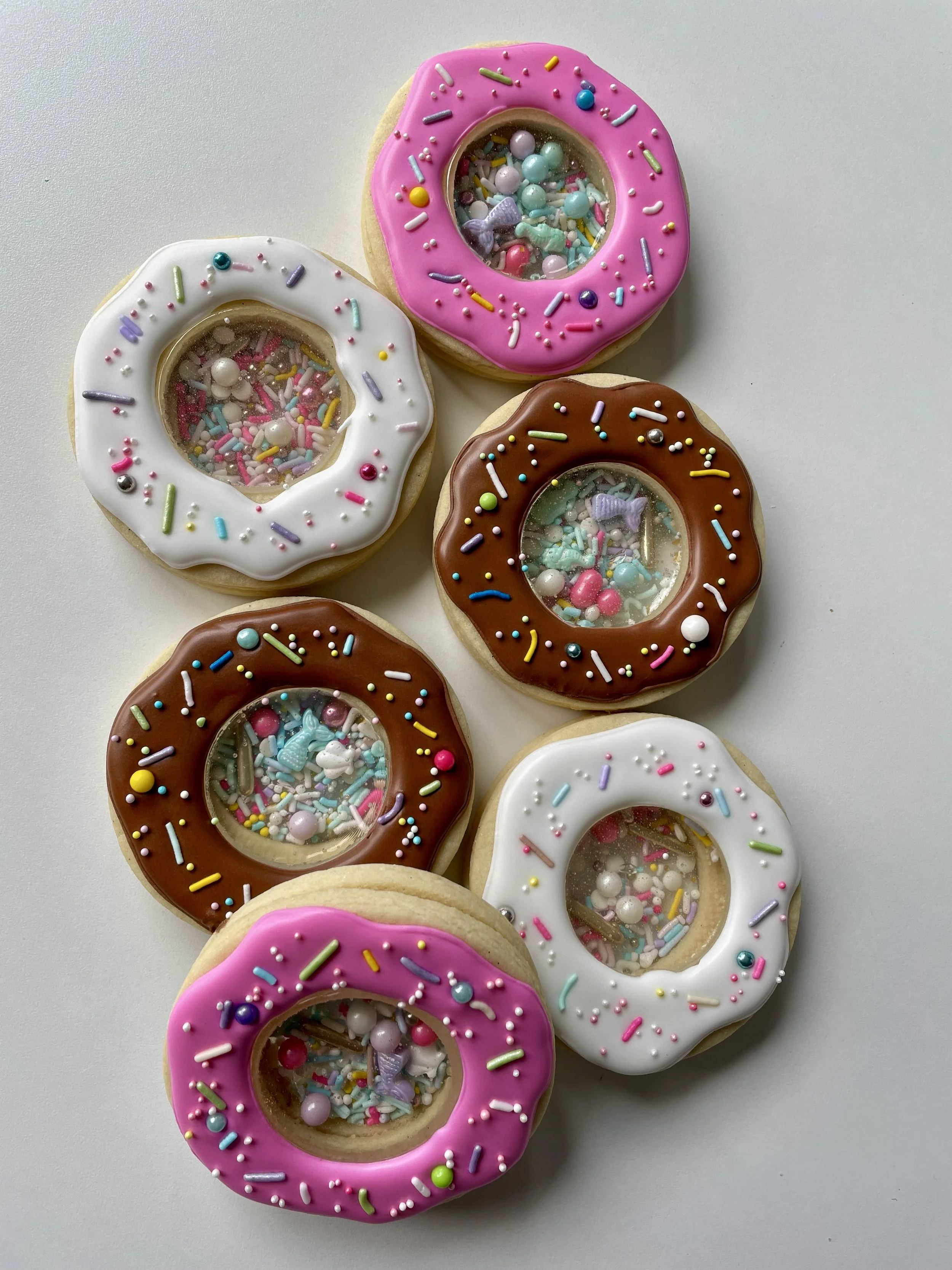 Six decorated donuts with colorful sprinkles and toppings, arranged on a white surface.