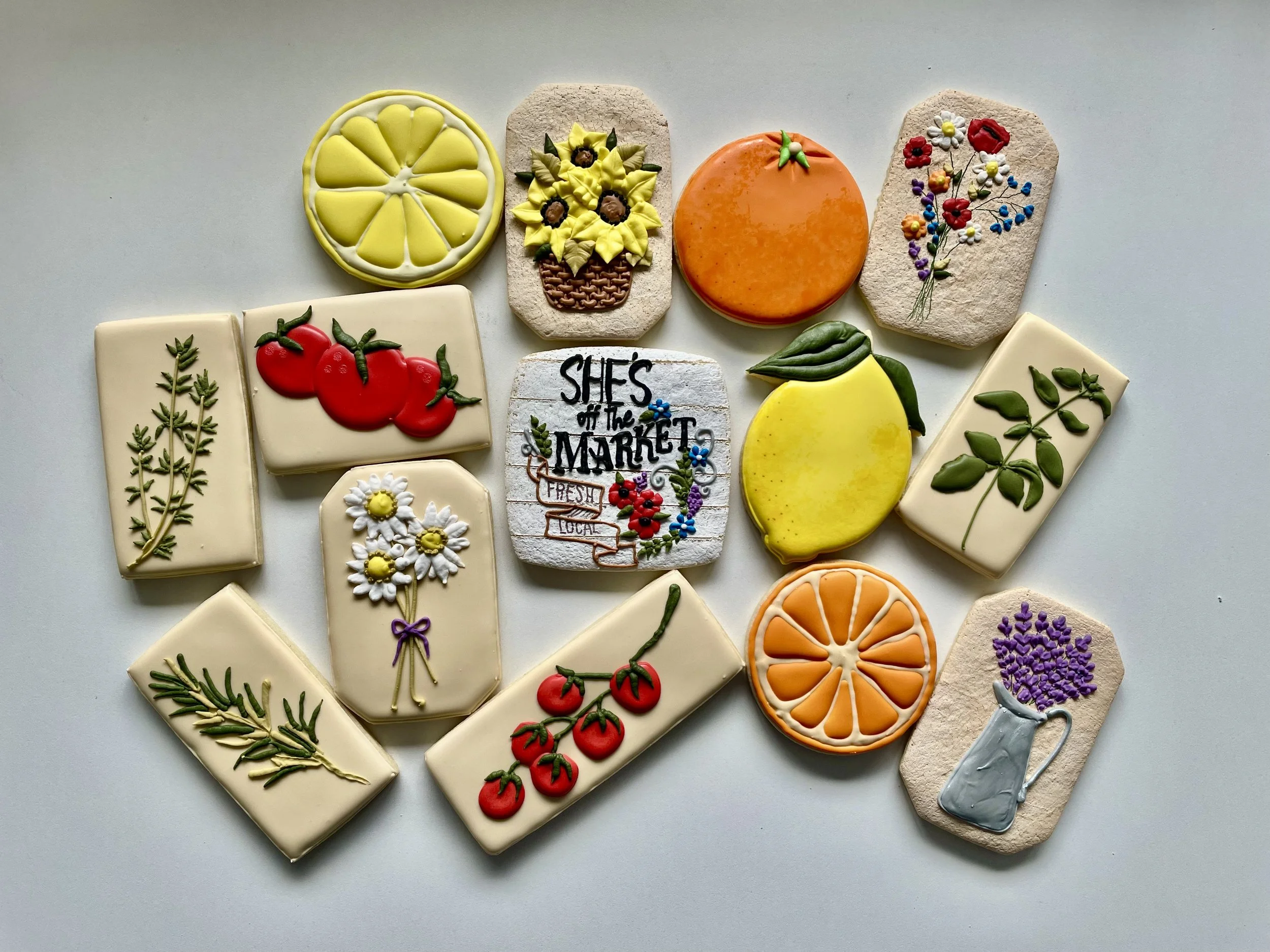 Collection of decorated cookies featuring fruits, flowers, herbs, and a sign that reads 'She's off the market' with colorful embroidery details.