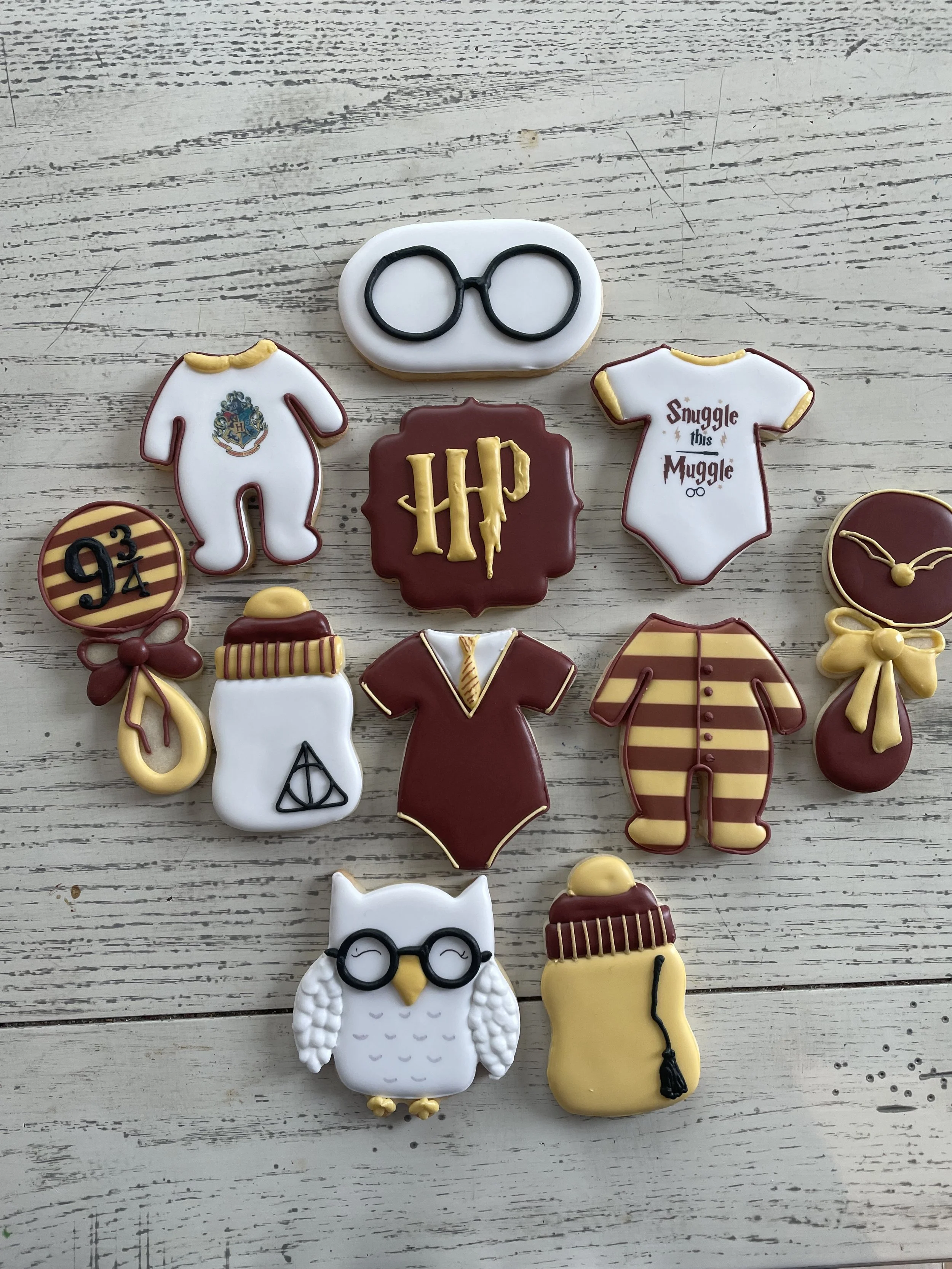 Decorated cookies inspired by Harry Potter, including glasses, a scar, a snitch, a potion bottle, a broomstick, a robe, and a clock, arranged on a wooden surface.