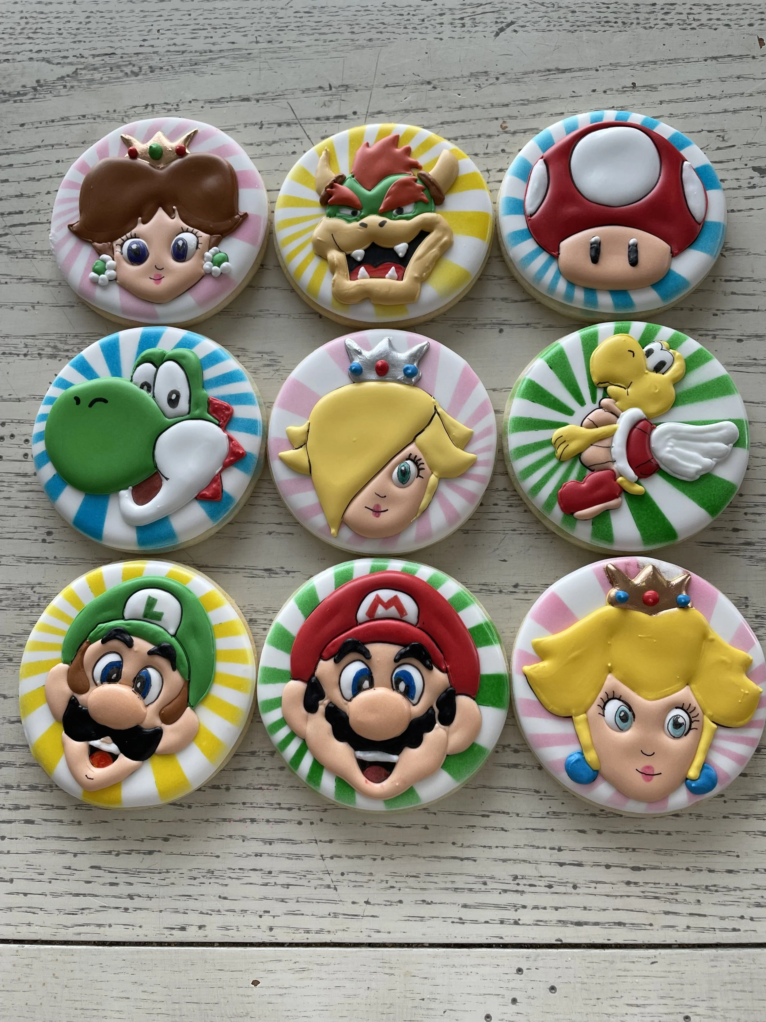 Decorative cookies featuring characters from the Super Mario video game series, including Princess Peach, Bowser, Mushroom, Yoshi, Princess Daisy, Toad, Luigi, Mario, and Princess Peach with a crown.