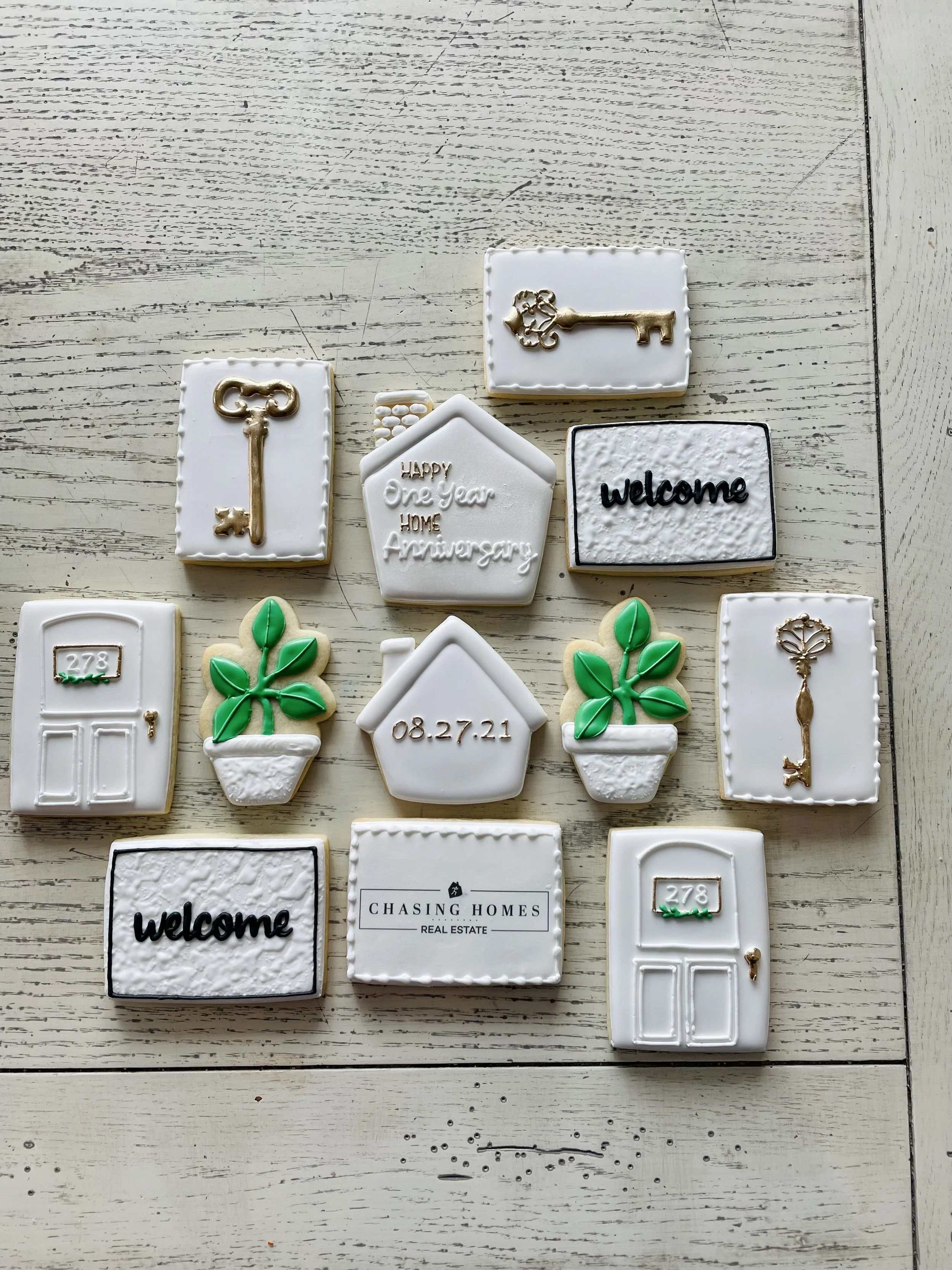 Collection of decorated cookies with keys, plants, doors, welcome signs, and house numbers on a white wooden surface.