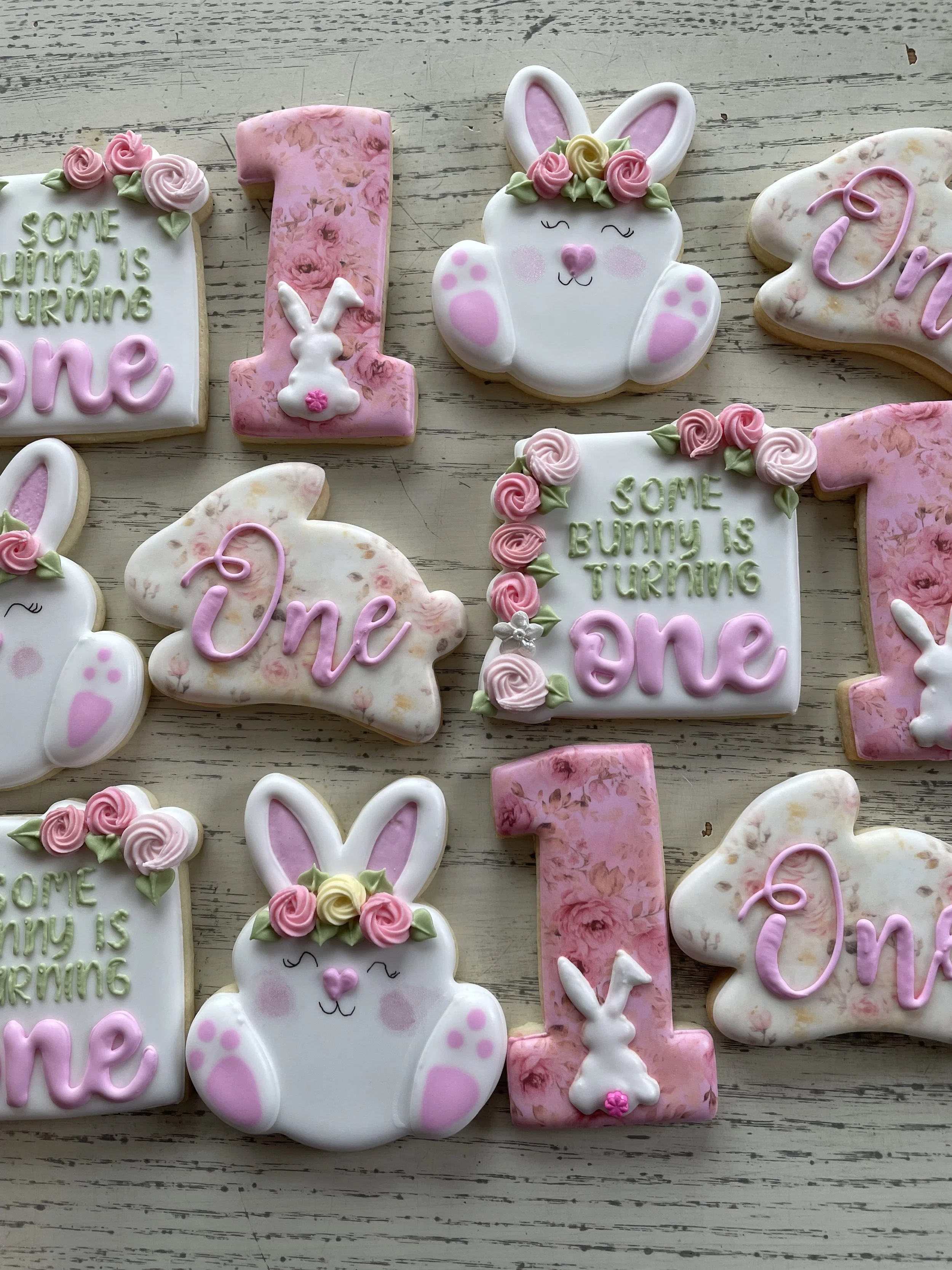 Decorative cookies with Easter Bunny and number one theme, pink, white, and green frosting, on a white wooden surface.