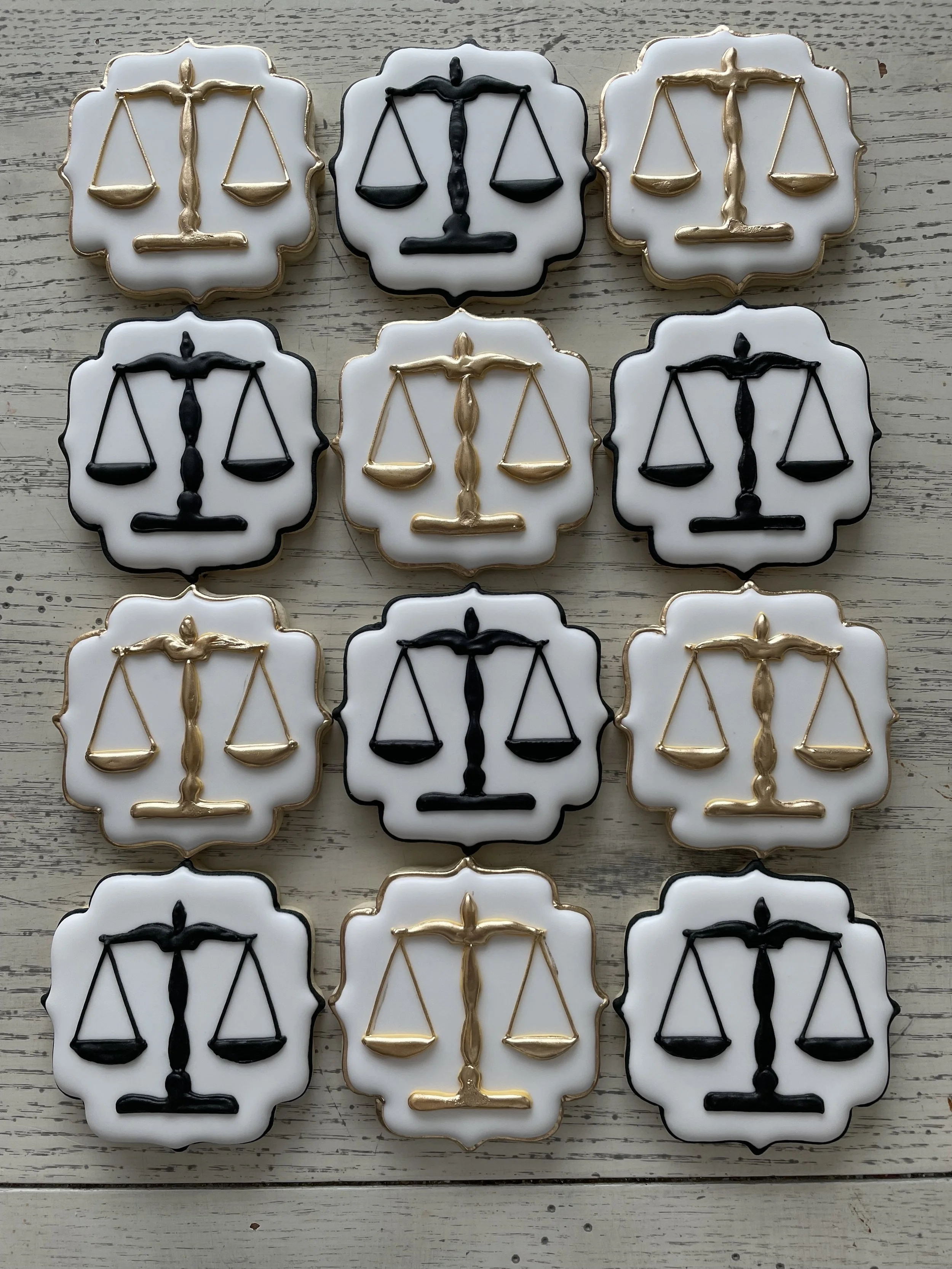 Set of decorative cookies with black and gold scale symbols on white background, arranged in a grid pattern on a wooden surface.