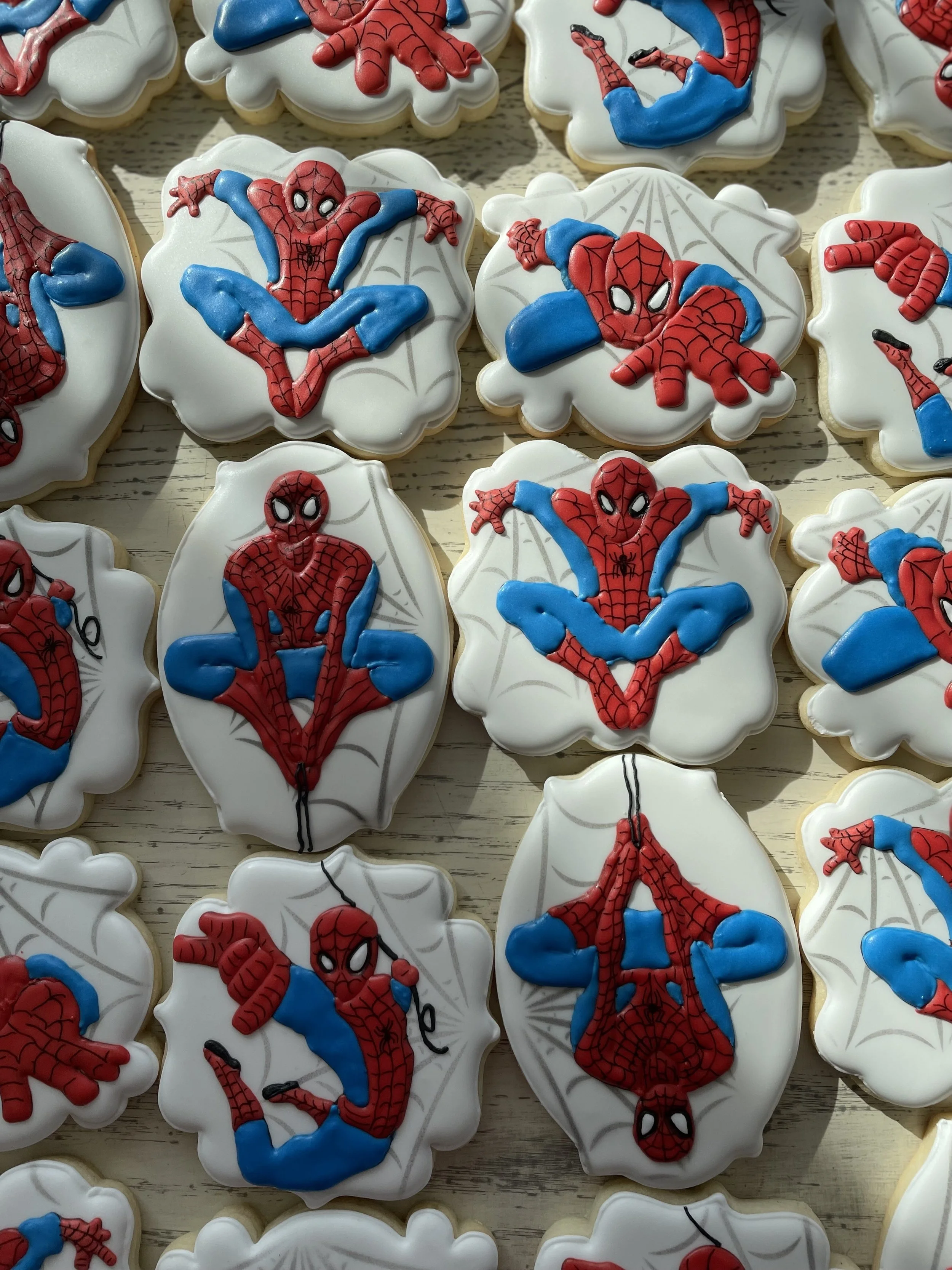 Cookies decorated with Spiderman designs in various poses on white icing with web patterns.