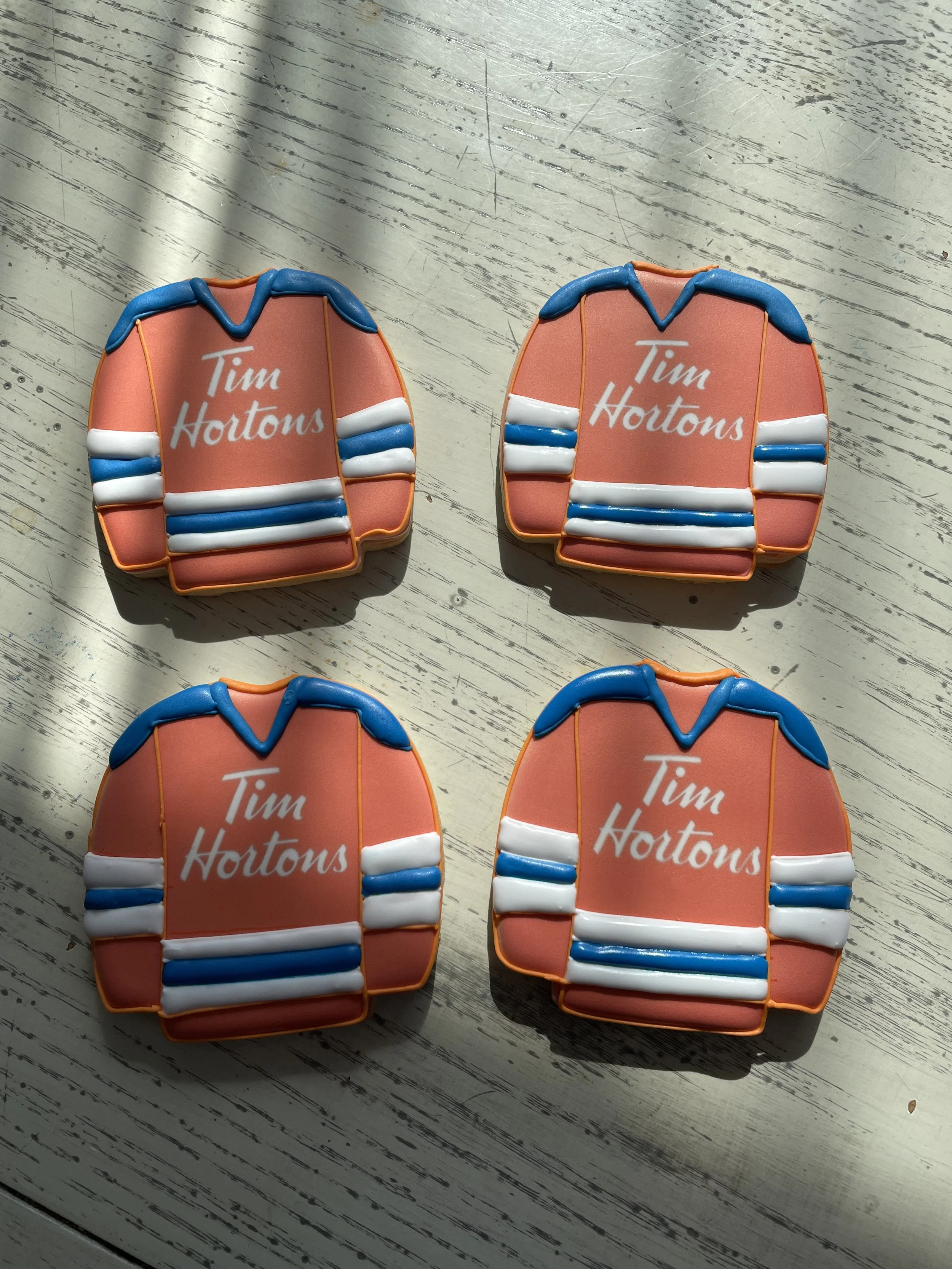 Four decorated cookies designed to resemble orange and blue sports jerseys with the words 'Tim Hortons' written on them, placed on a wooden surface.