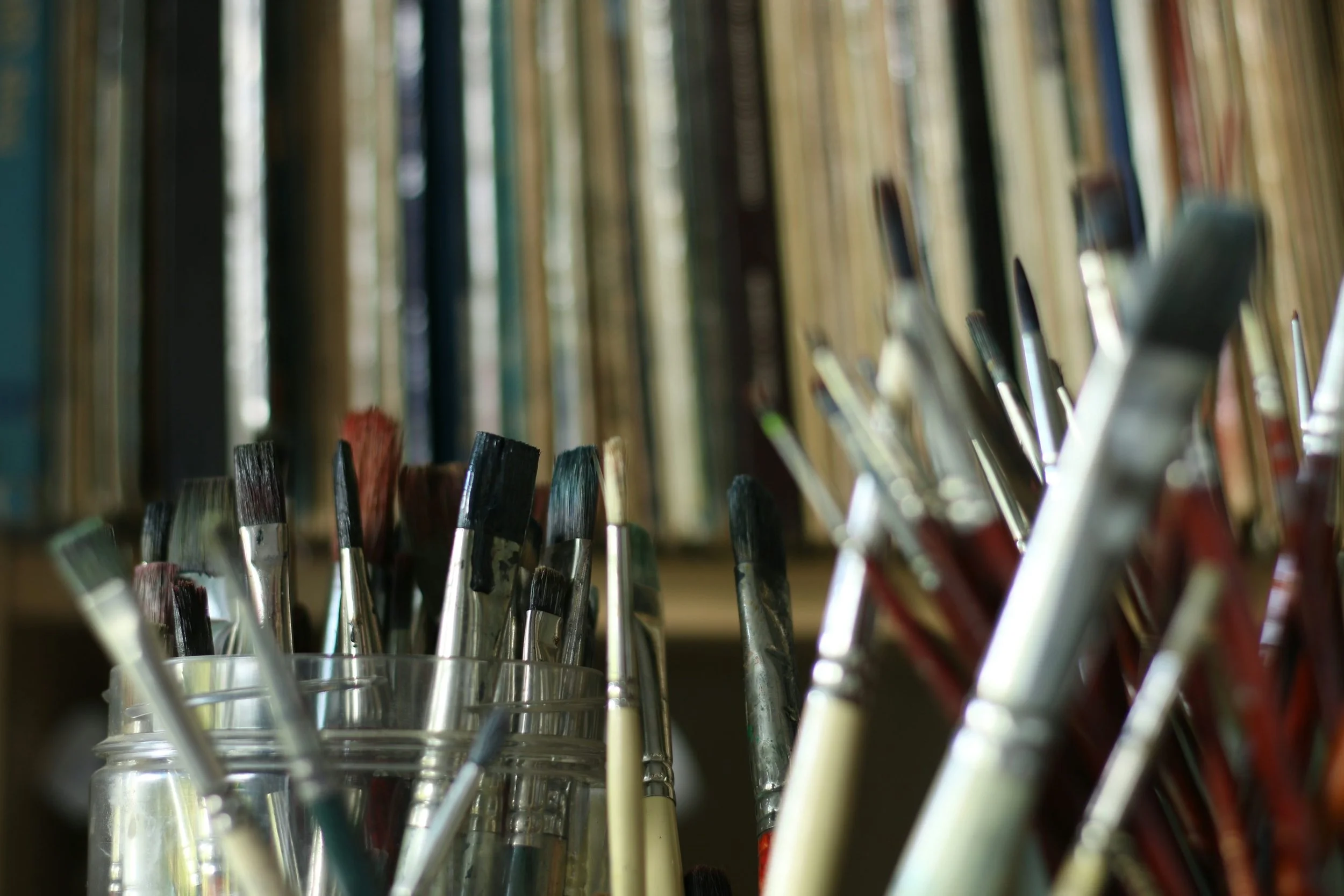 Worn paintbrushes fill clear glass jars, with a softly blurred background.
