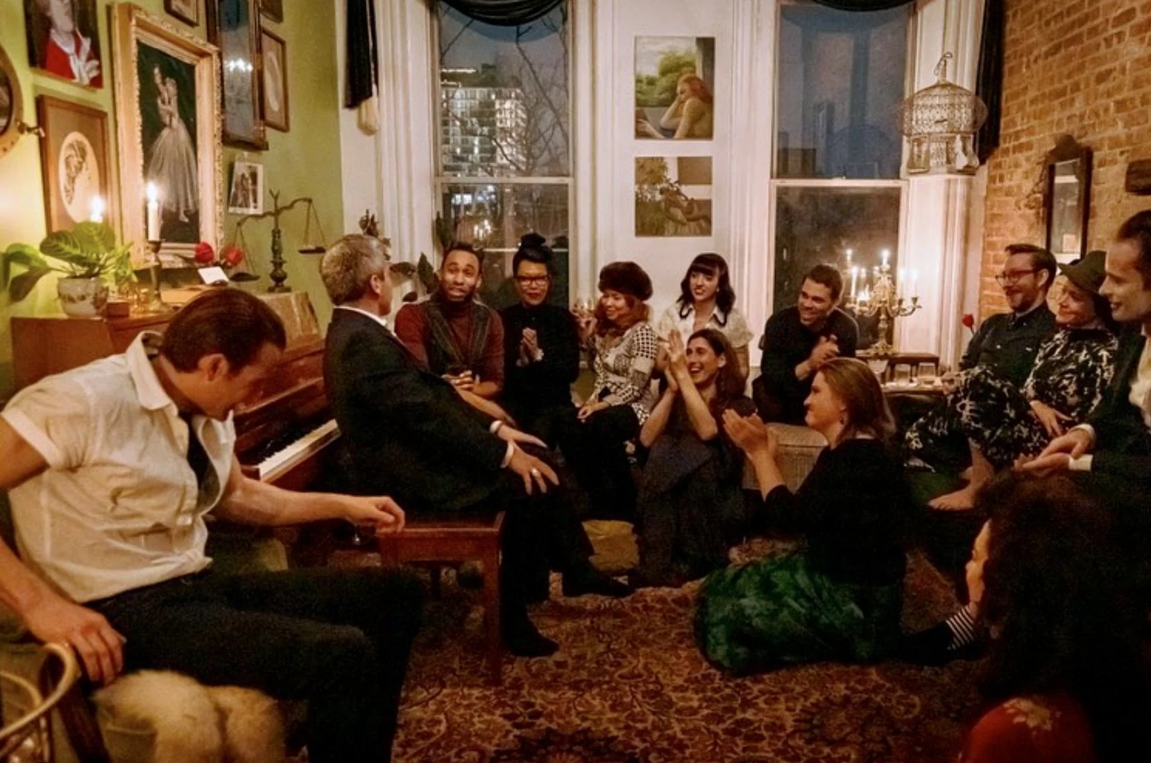 A group of people gathered in a cozy, decorated living room, sitting on the floor and on furniture, engaging in conversation and laughter during a social gathering.