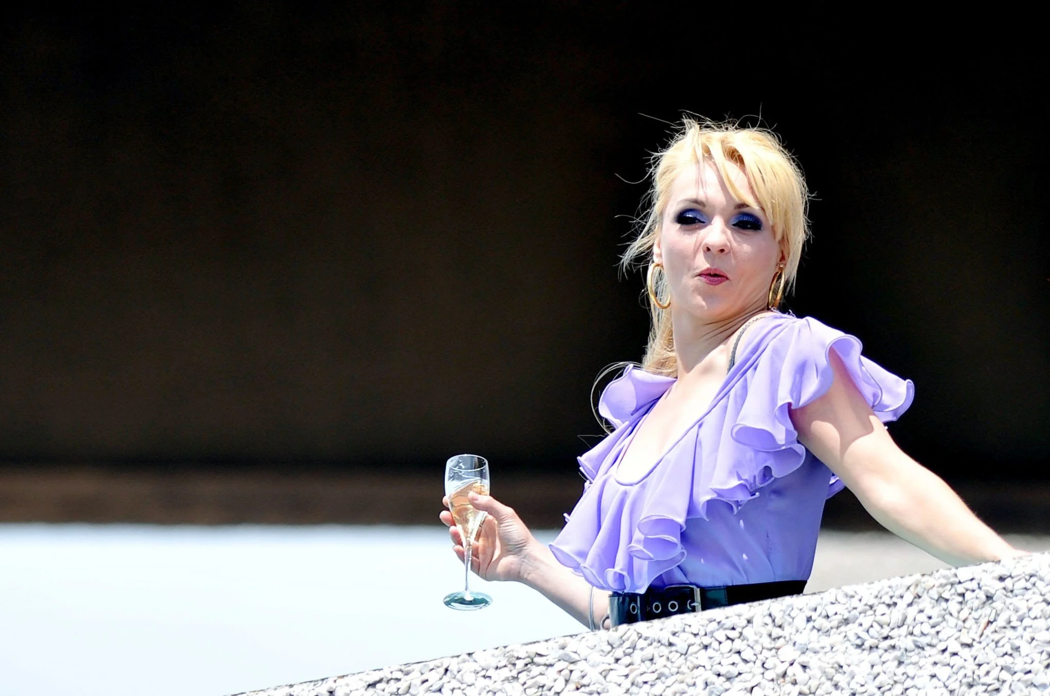 Woman with blonde hair in a lilac ruffled dress holding a glass of champagne.