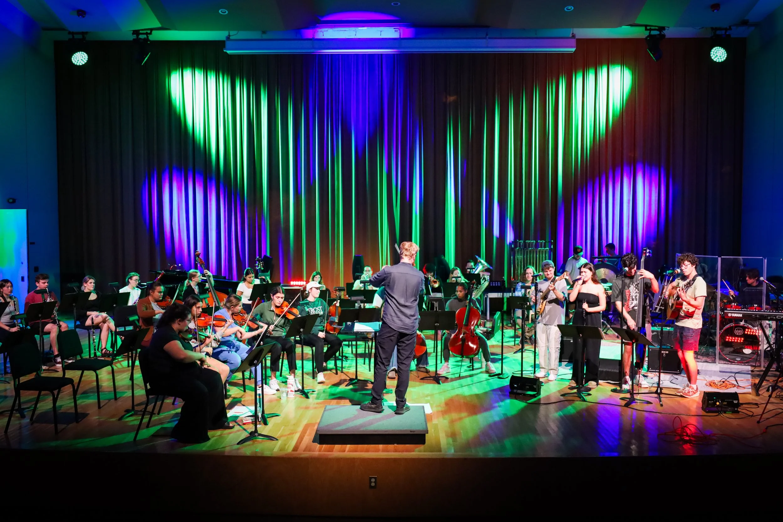 Rock Symphonic Orchestra performing on stage with colorful lighting and a conductor leading the musicians.