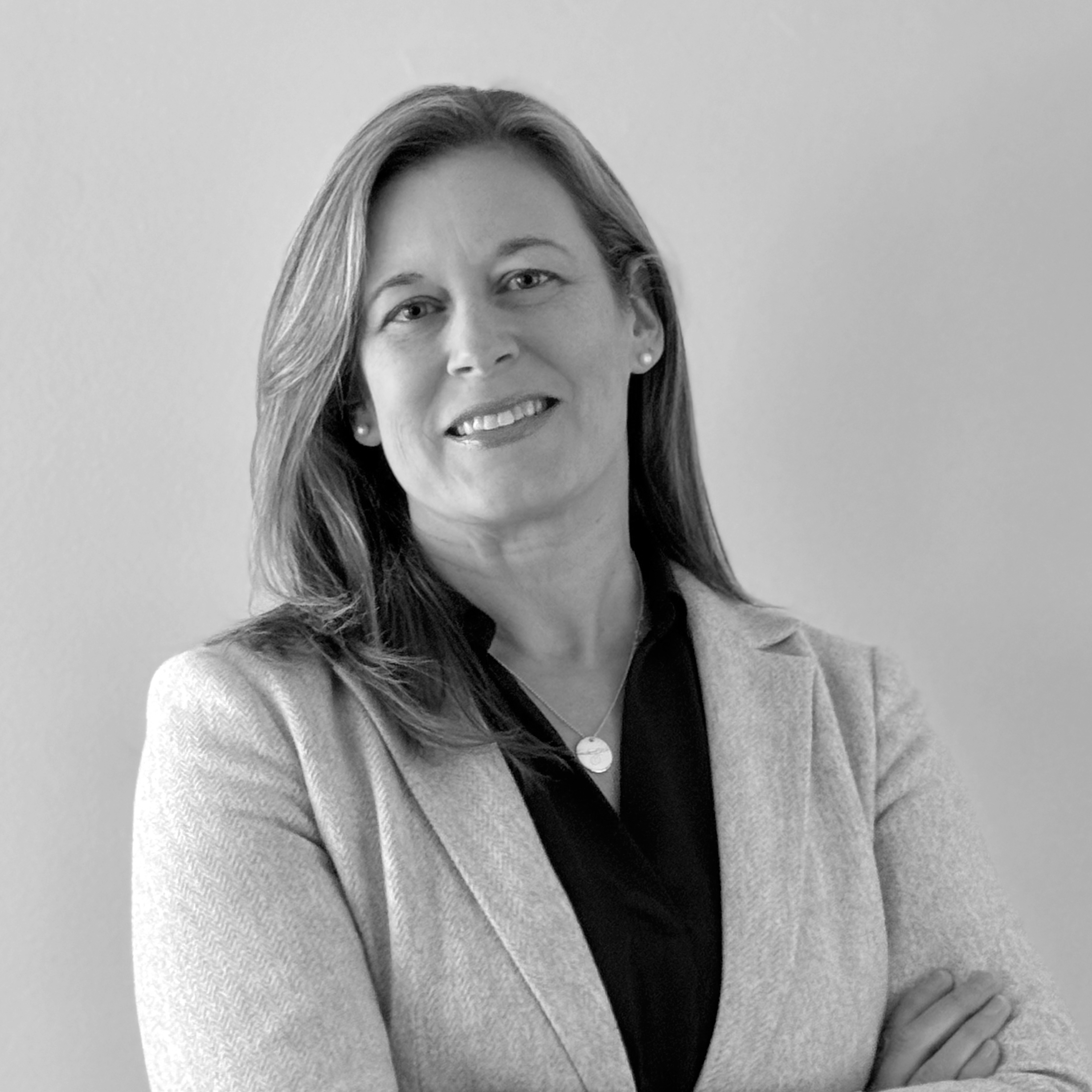Black and white portrait of a smiling woman with medium-length hair, wearing a light blazer over a dark top, standing against a plain background.