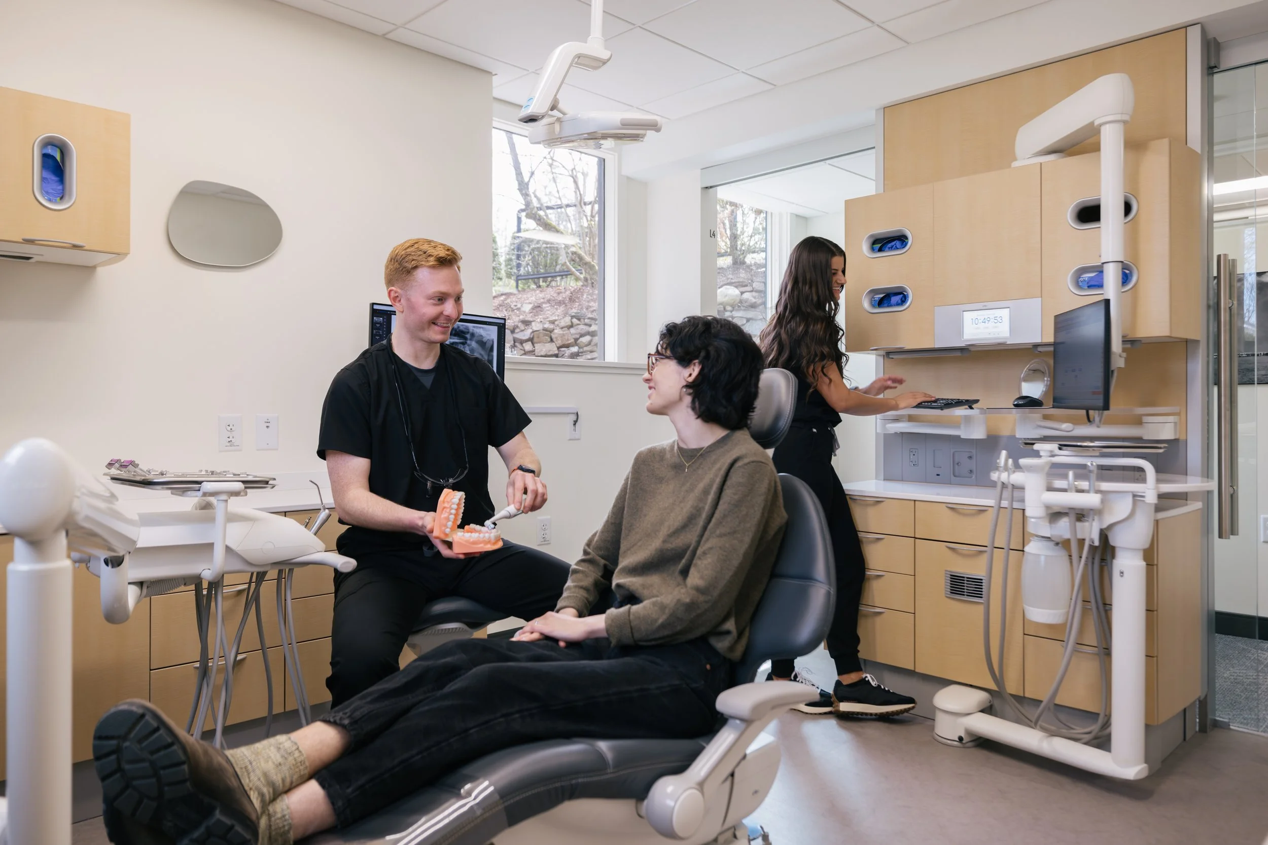 Dental office with a patient and a dental professional engaging in conversation, a dental model on the dental chair, and dental equipment around the room.