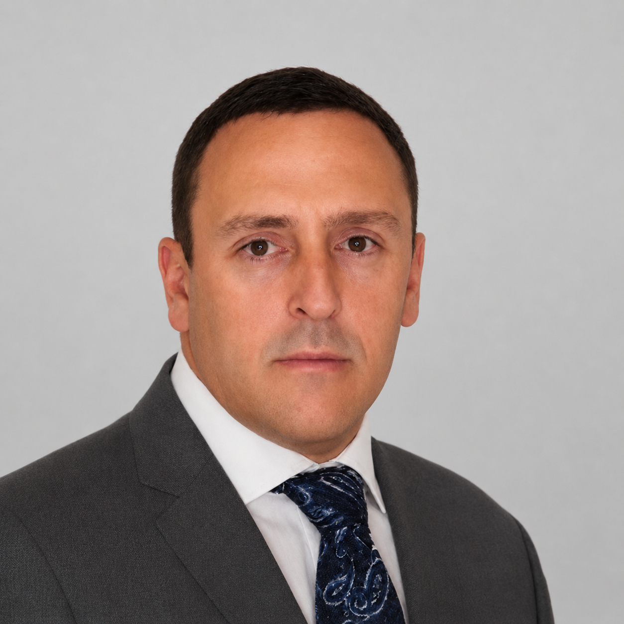 Professional headshot of a man in a suit and tie against a gray background.