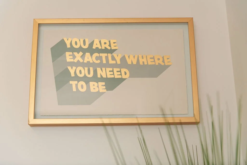 Framed wall decor with the text "You are exactly where you need to be" in beige letters on light background with shadows.