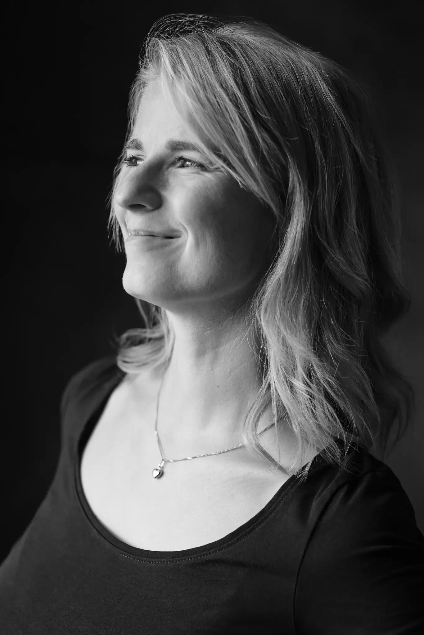 Schwarz-weiß Portrait einer lächelnden Frau mit mittelblondem, gewelltem Haar, die nach rechts schaut.