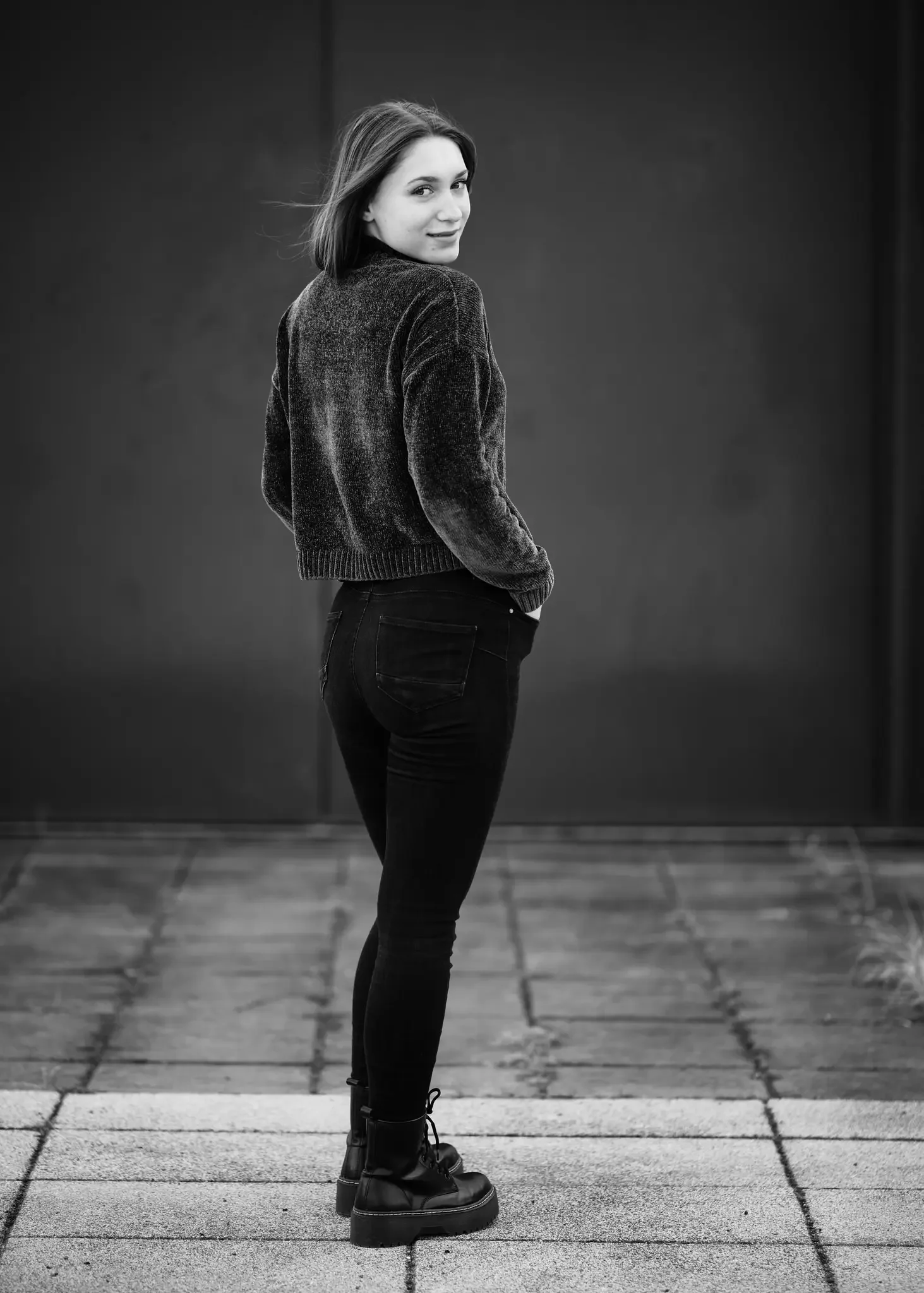 Schwarze und weiße Modefotografie einer jungen Frau, die auf einer gepflasterten Oberfläche steht und in die Kamera blickt.