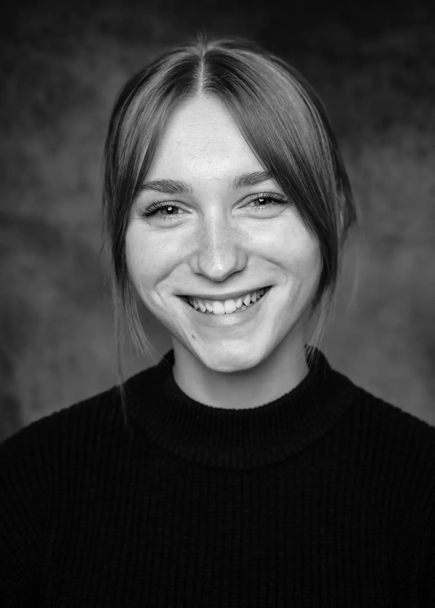 Schwarz-weiß Porträt einer lachenden jungen Frau mit mittellangen Haaren, die einen schwarzen Rollkragenpullover trägt.