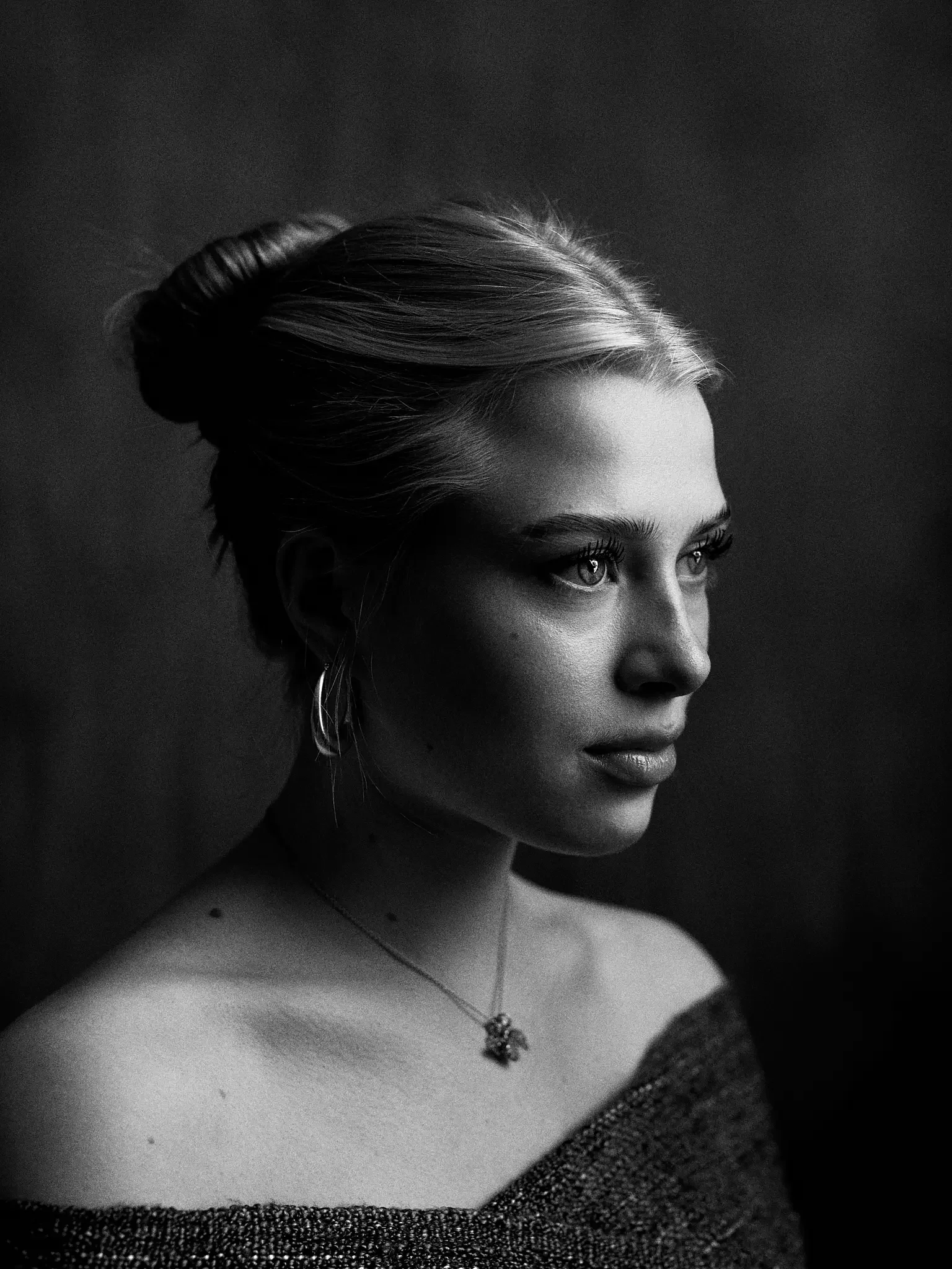 Schwarze und weiße Portraitaufnahme einer jungen Frau mit blonder, gebundener Frisur, seitlichem Blick, Ohrringen und einem neongelben T-Shirt.