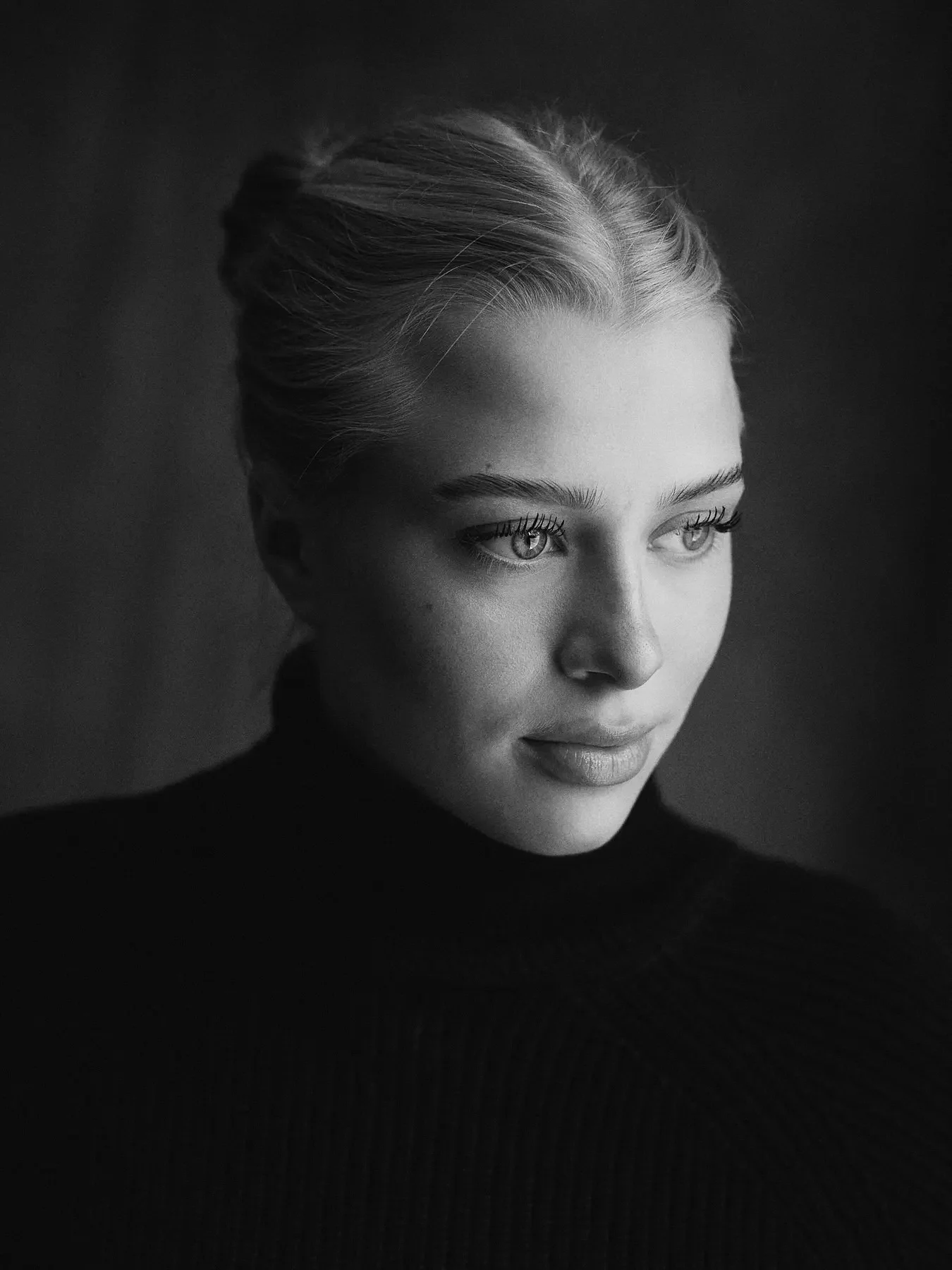 Schwarz-weiß Porträt einer jungen Frau mit gegelten Haaren, die einen schwarzen Pullover trägt, Blick nach rechts, sanfter Ausdruck.