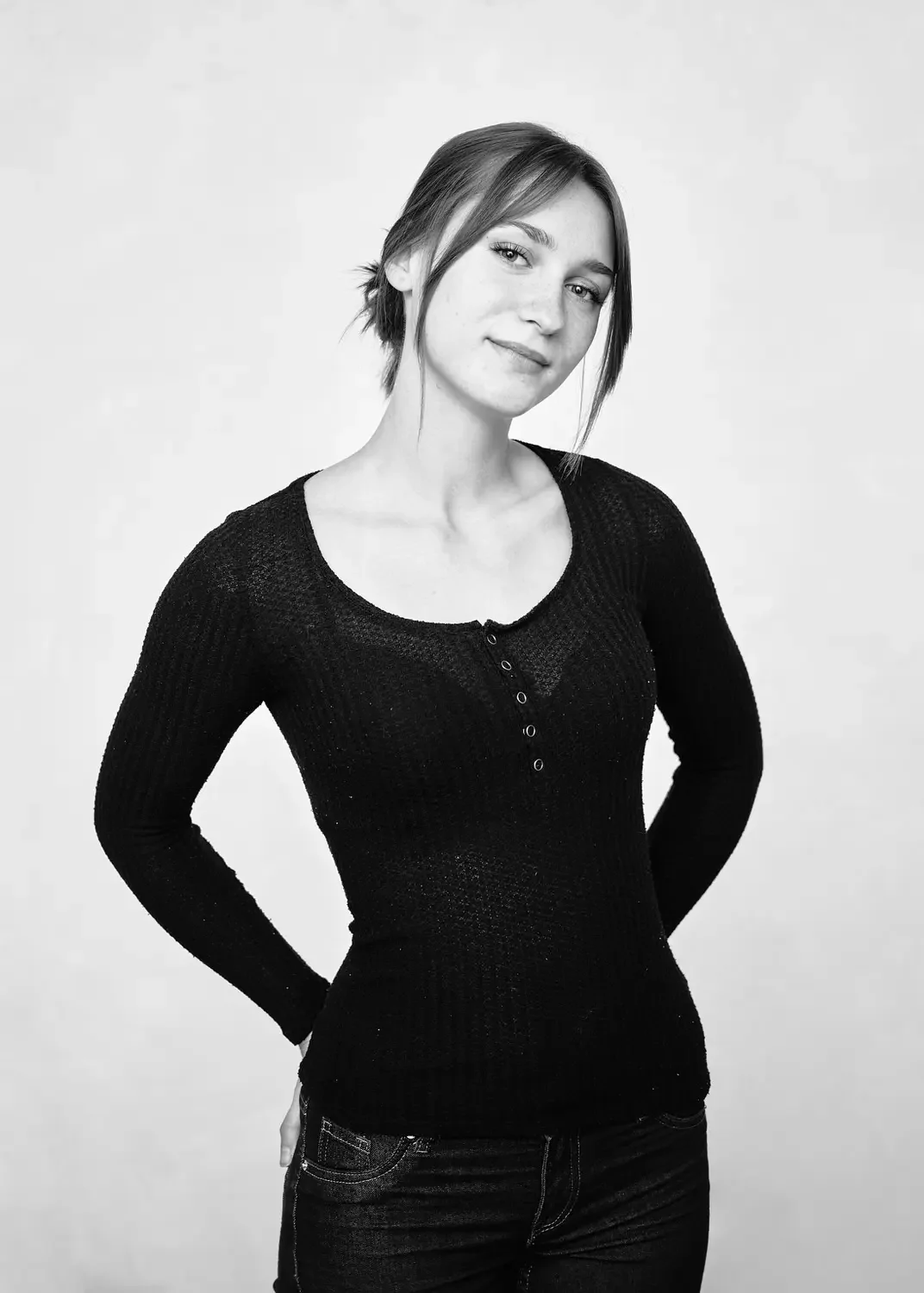 Schwarz-weiß Foto eines jungen Mädchens mit dunkler Top, lächelnd, vor hellem Hintergrund.