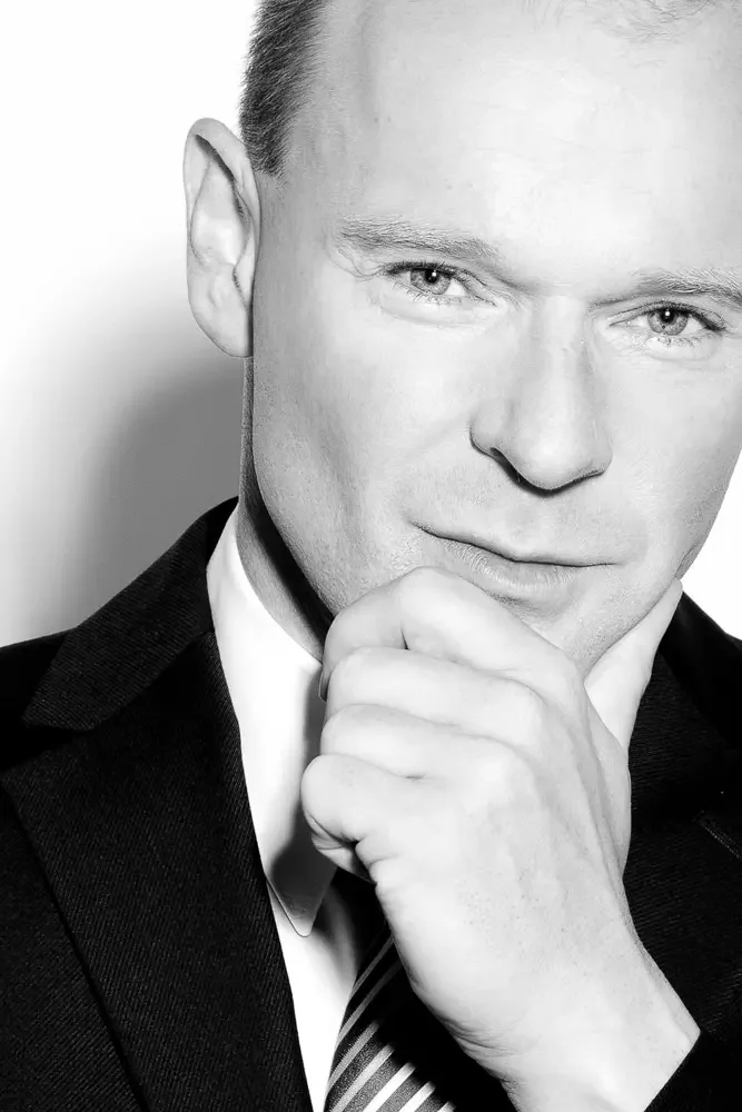 Nahaufnahme eines Mannes in Anzug mit Krawatte, der nachdenklich die Hand an den Mund legt, im schwarzen und weißen Farbstil.