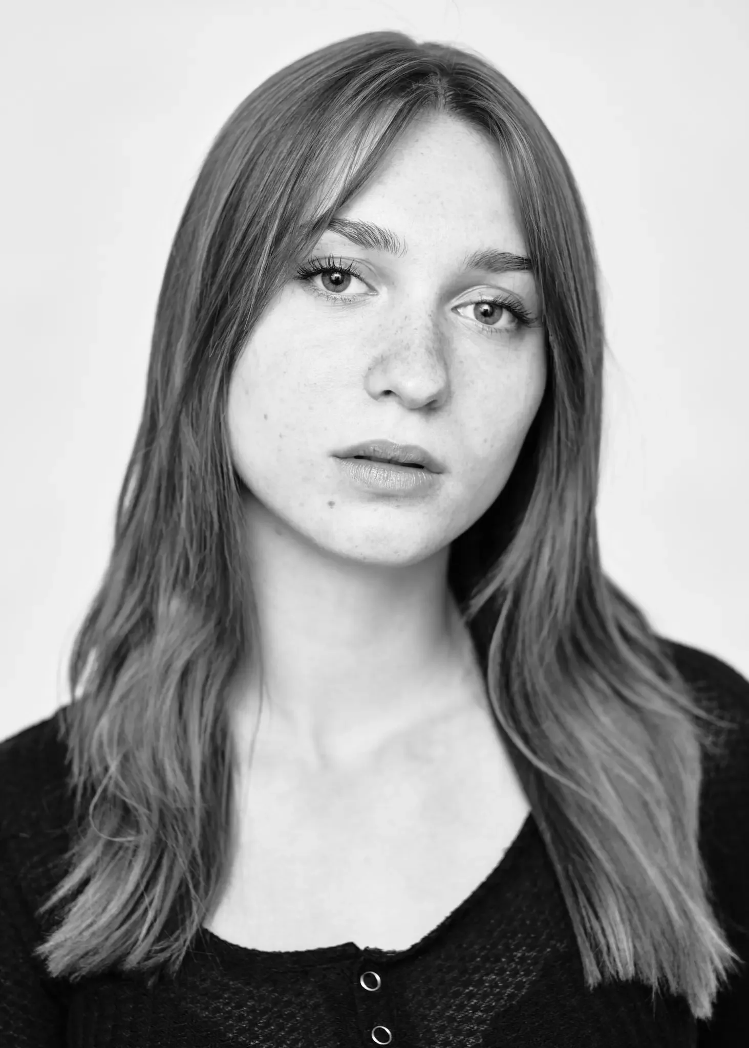 Schwarz-weiß Porträt eines jungen Mädchens mit mittellangen, glatten Haaren, die ihre Schultern bedecken, und einem entspannten Gesichtsausdruck, vor hellem Hintergrund.