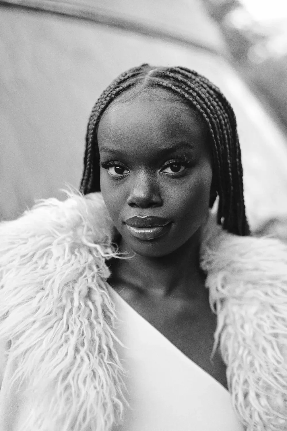 Schwarz-weiß-Fotografie einer schwarzen Frau mit geflochtenem Haar, die eine flauschige Jacke trägt.