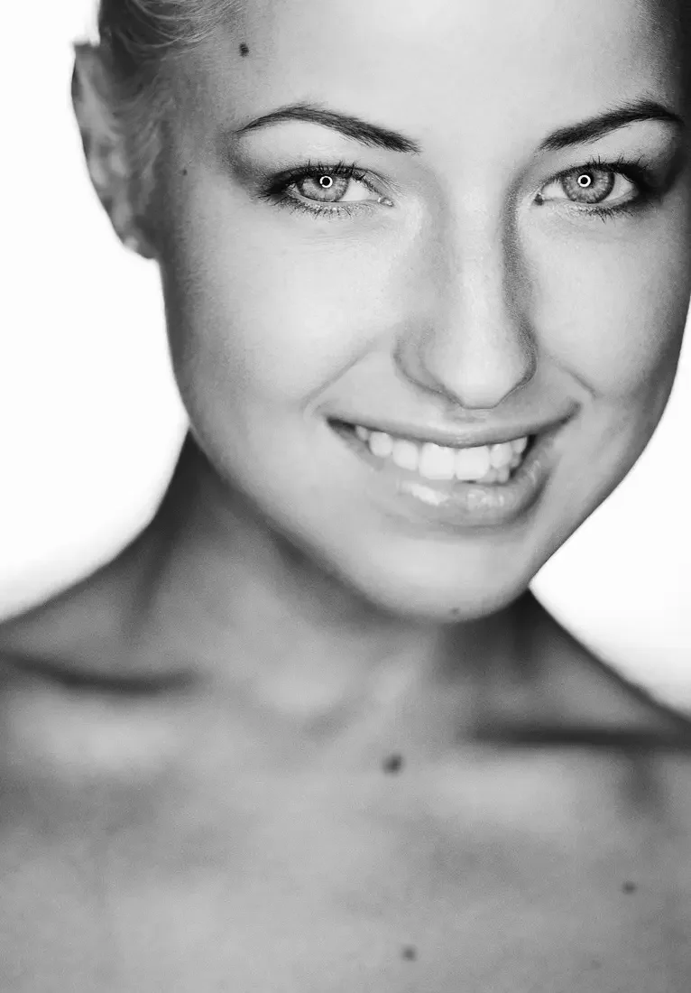 Schwarz-weiß-Porträt einer jungen Frau mit blonden Haaren, die lachen und einen freundlichen Ausdruck zeigt.