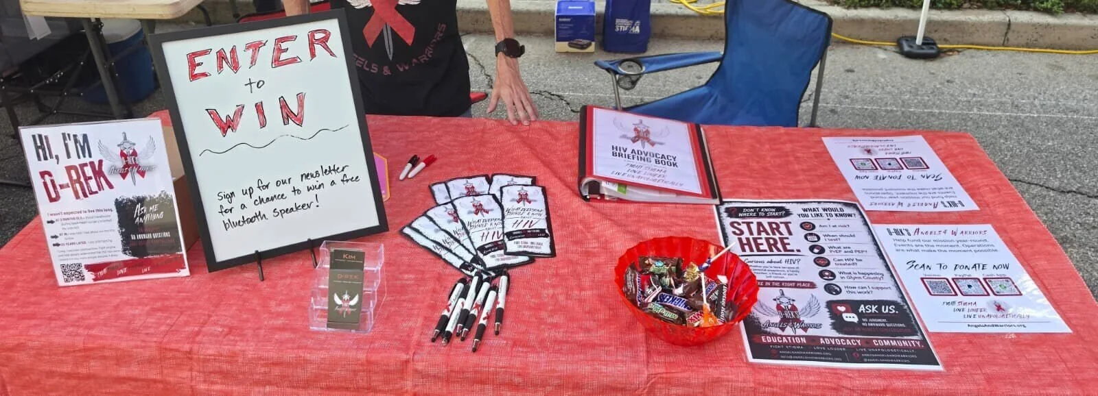 Angels & Warriors First Friday table with an Enter to Win sign, HIV info flyers, and a bowl of candy