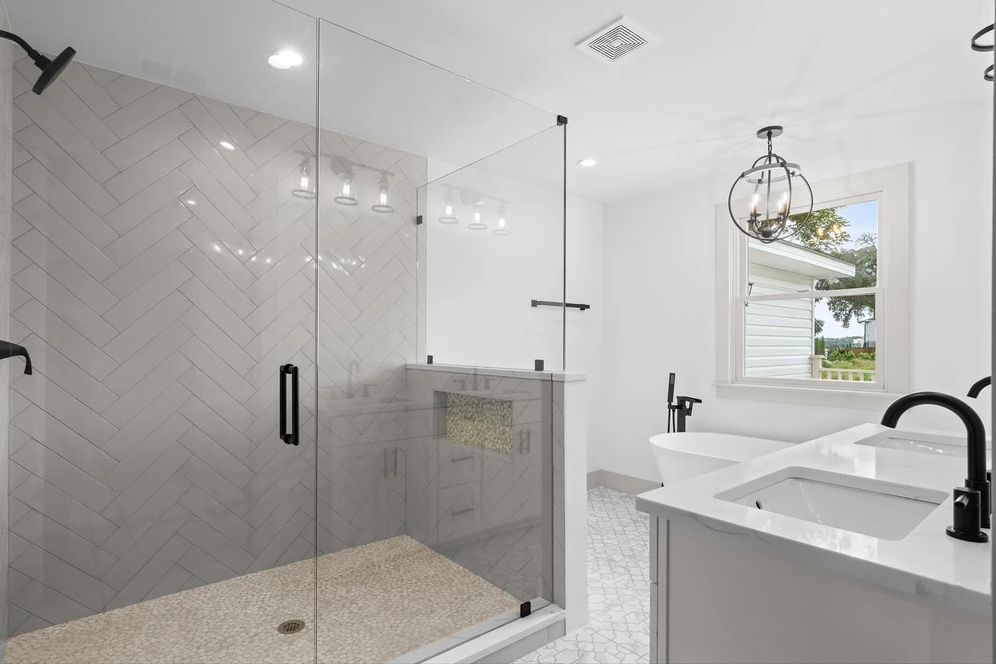 Timeless design meets modern luxury. This Marsh Point Developers bathroom features a spacious glass shower with herringbone tile, a freestanding soaking tub, and bold black fixtures that bring it all together. Every detail&mdash;from the custom tile 