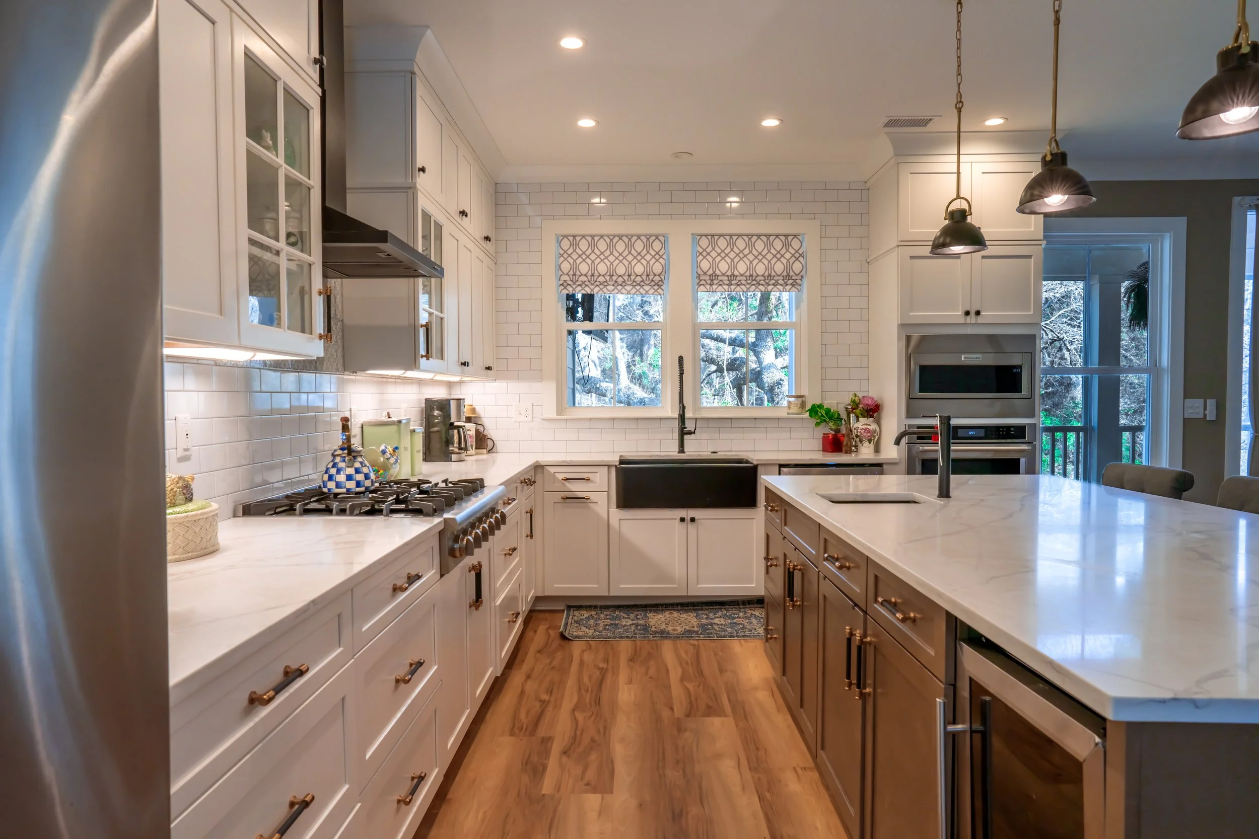 Modern kitchen with white cabinets, a large marble island with dark wood base, white subway tile backsplash, black farmhouse sink, and a view of trees through the windows.