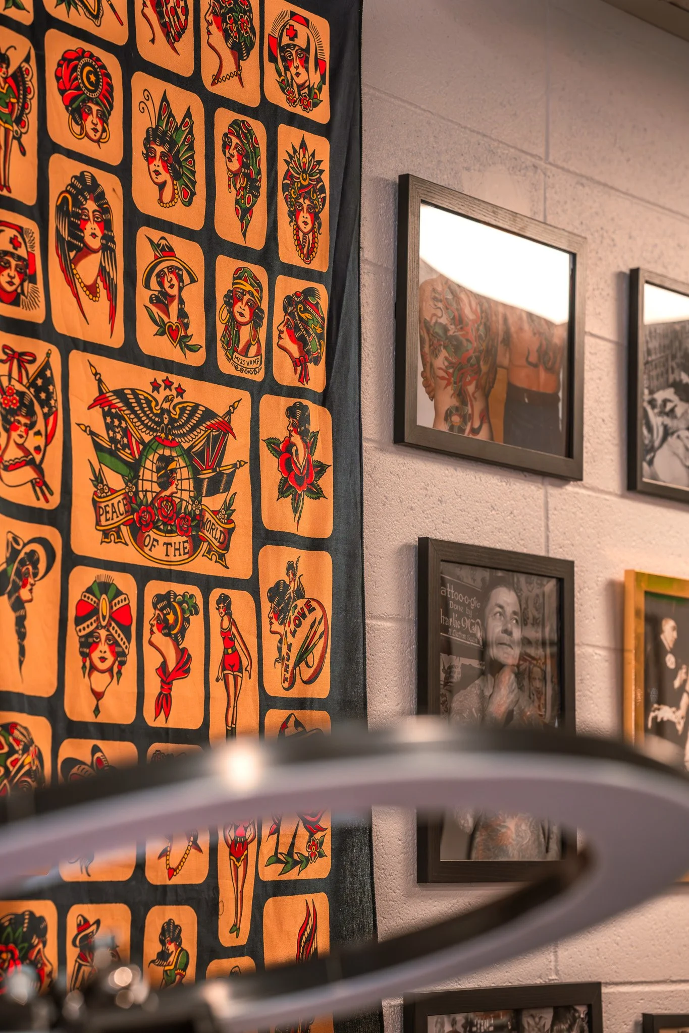 Wall decorated with tattoo art and framed photographs, including images of tattoos and a woman with tattoos on her upper body.