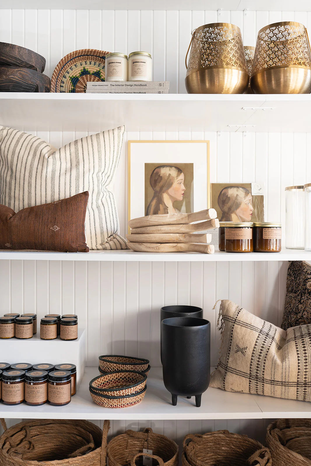 White shelves filled with home decor items, including pillows, paintings, baskets, candles, and jars, arranged in a minimalist style. Interior Design Guelph