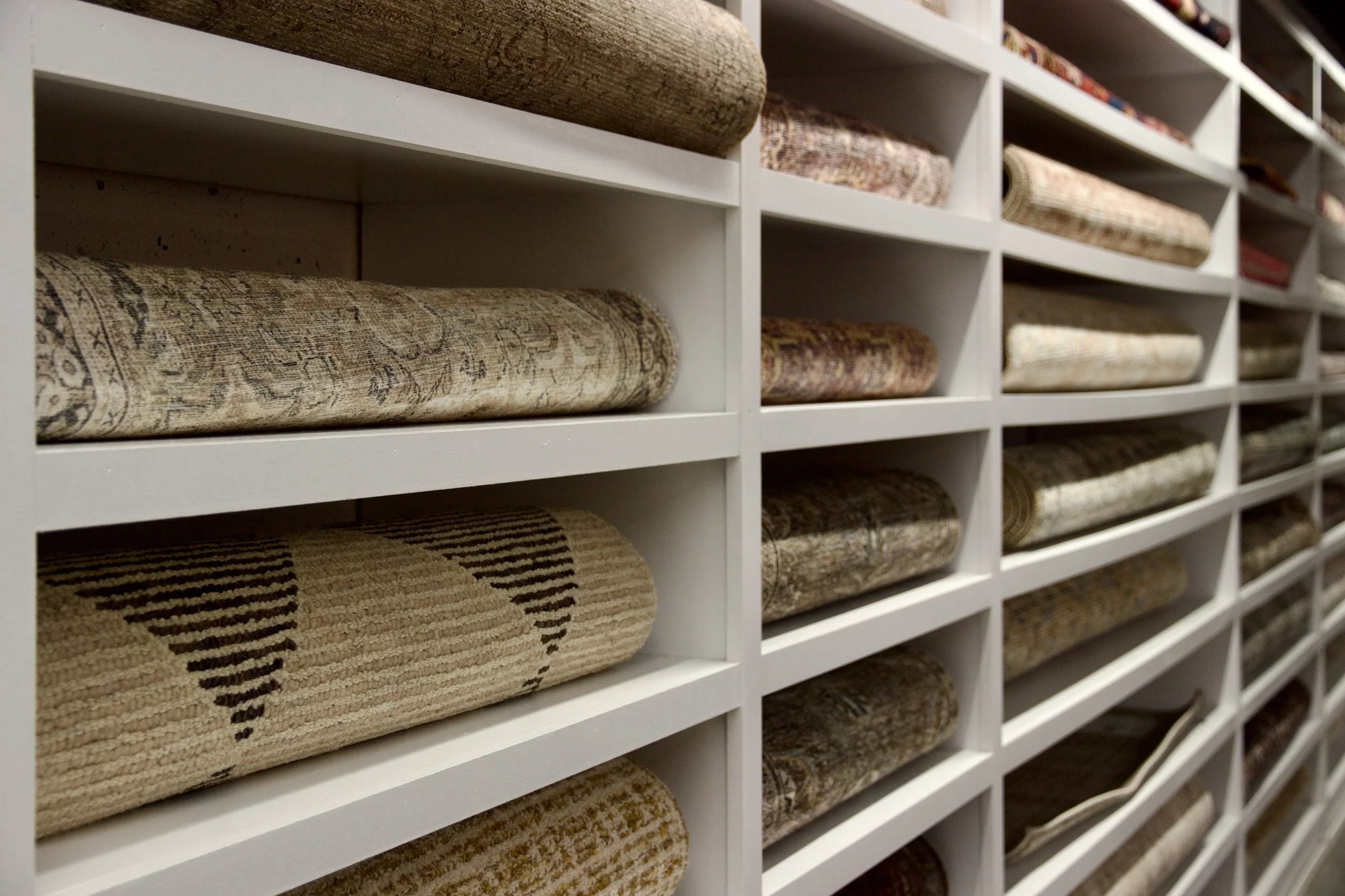 Rows of rolled-up rugs displayed on white shelves in a store. Interior Design Guelph