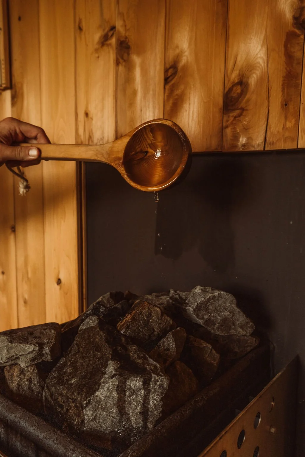 A person pouring water from a wooden ladle over rocks inside a sauna or steam room.