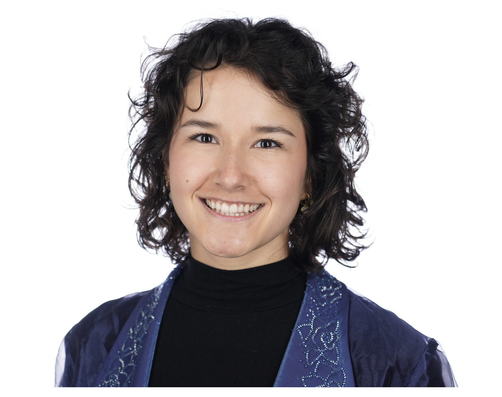 A person with short dark curly hair smiling