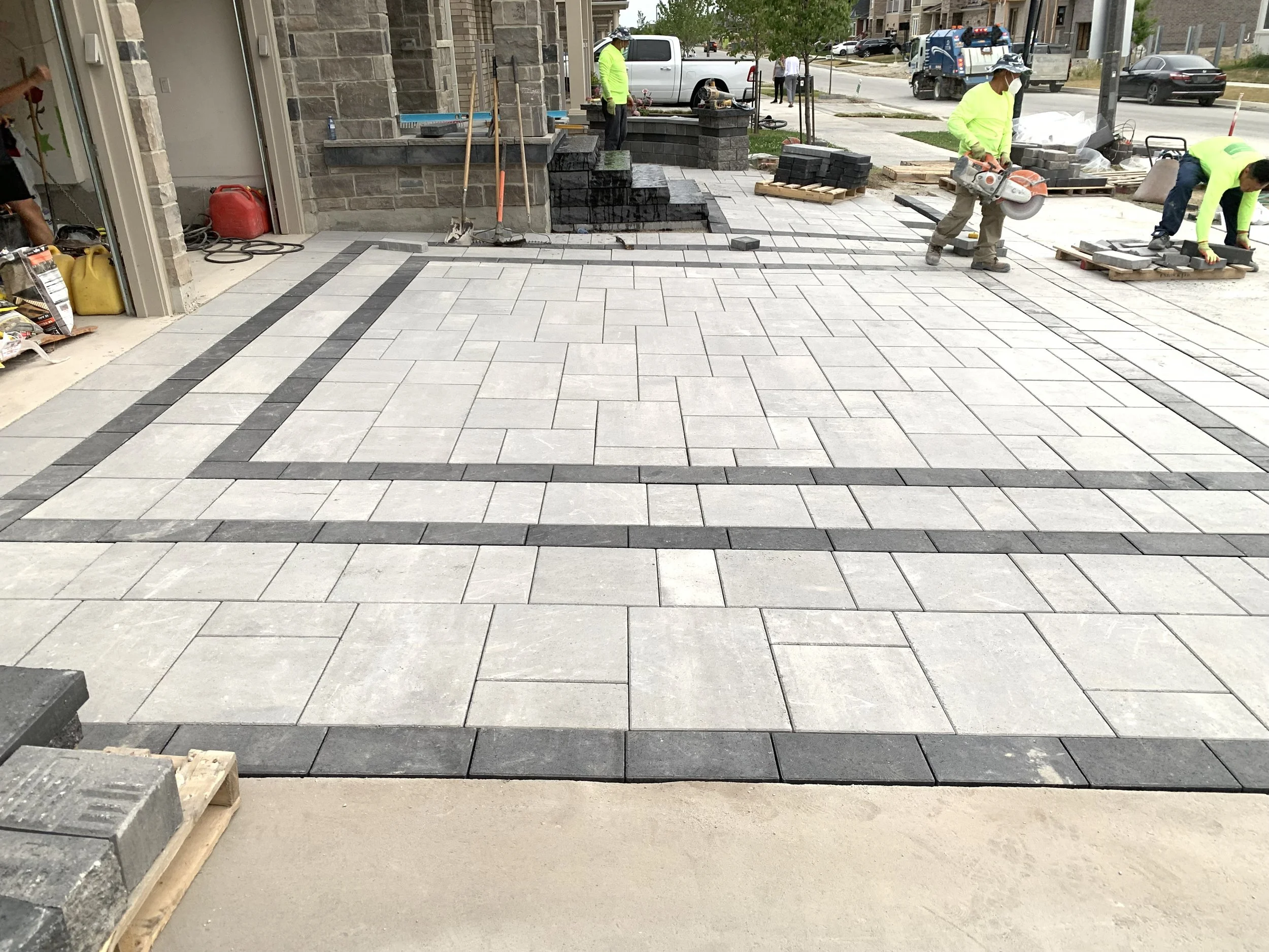Stone driveway installation with patterned gray tiles and workers using tools.