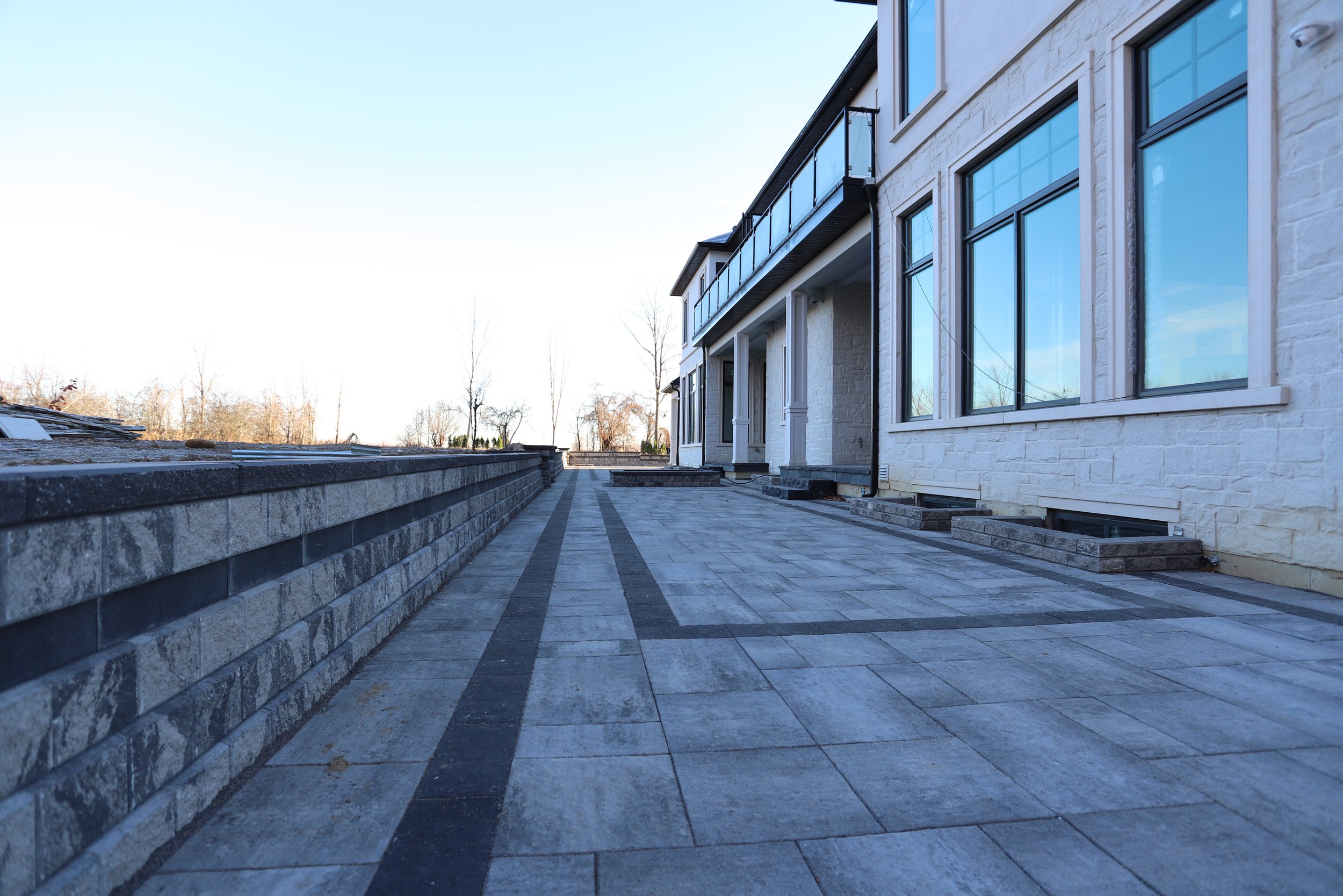 Modern house exterior with large patio, stone pathway, and retaining wall.
