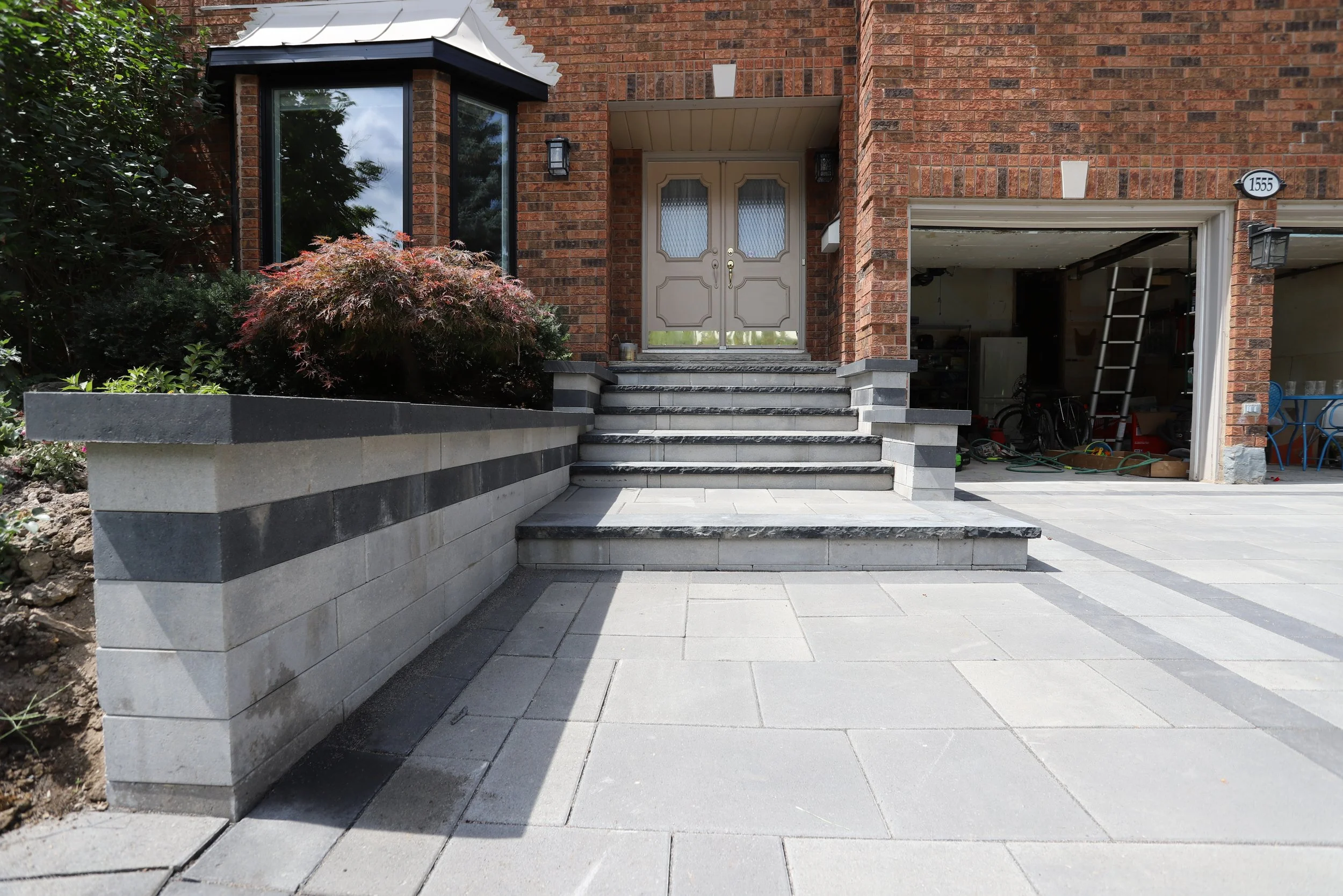 Brick house entrance with stairs, garage, and landscaped garden.