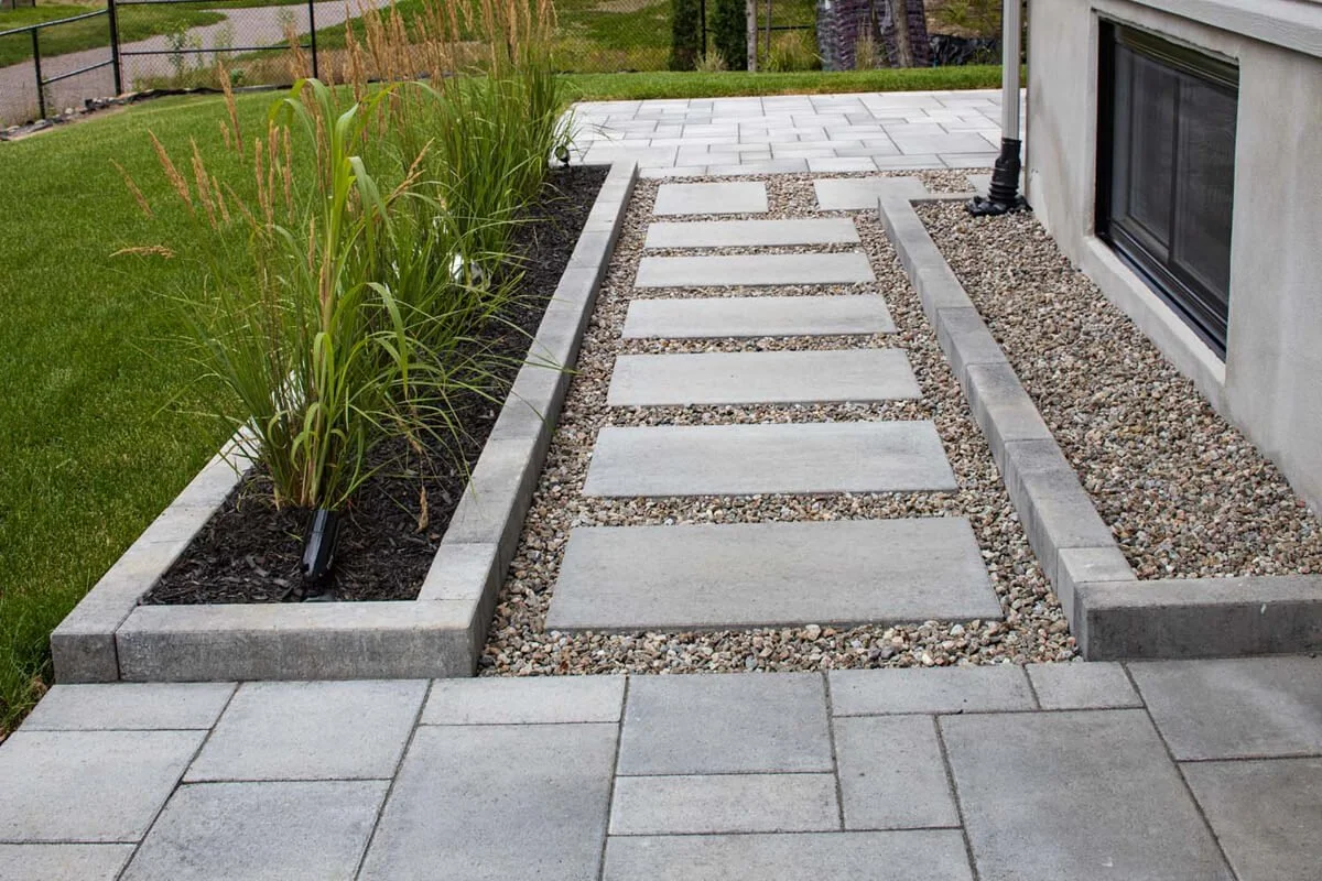 Modern backyard with concrete paver path, gravel, and ornamental grass landscaping.